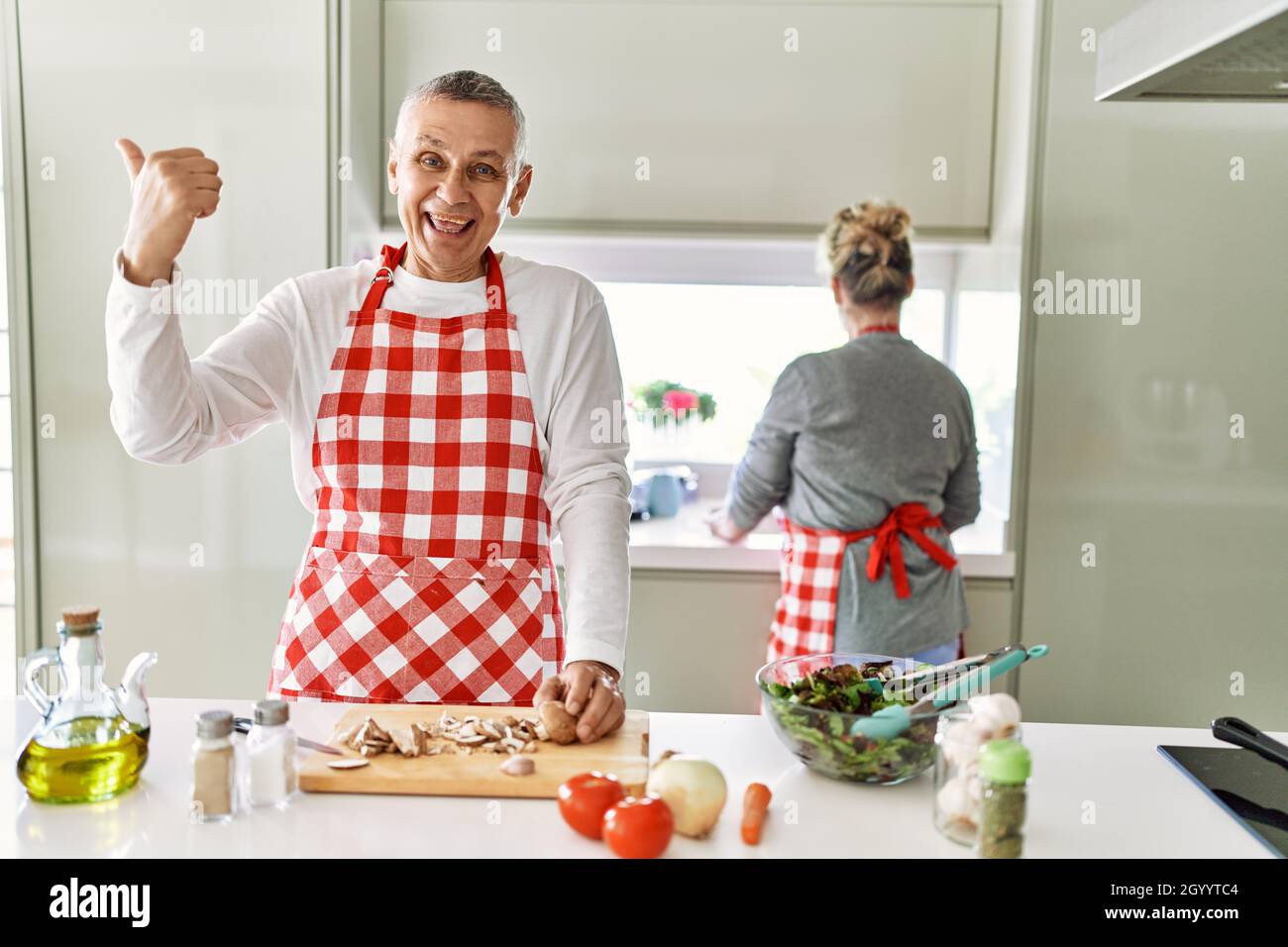 Middle age caucasian couple cooking healthy salad pointing thumb up to ...
