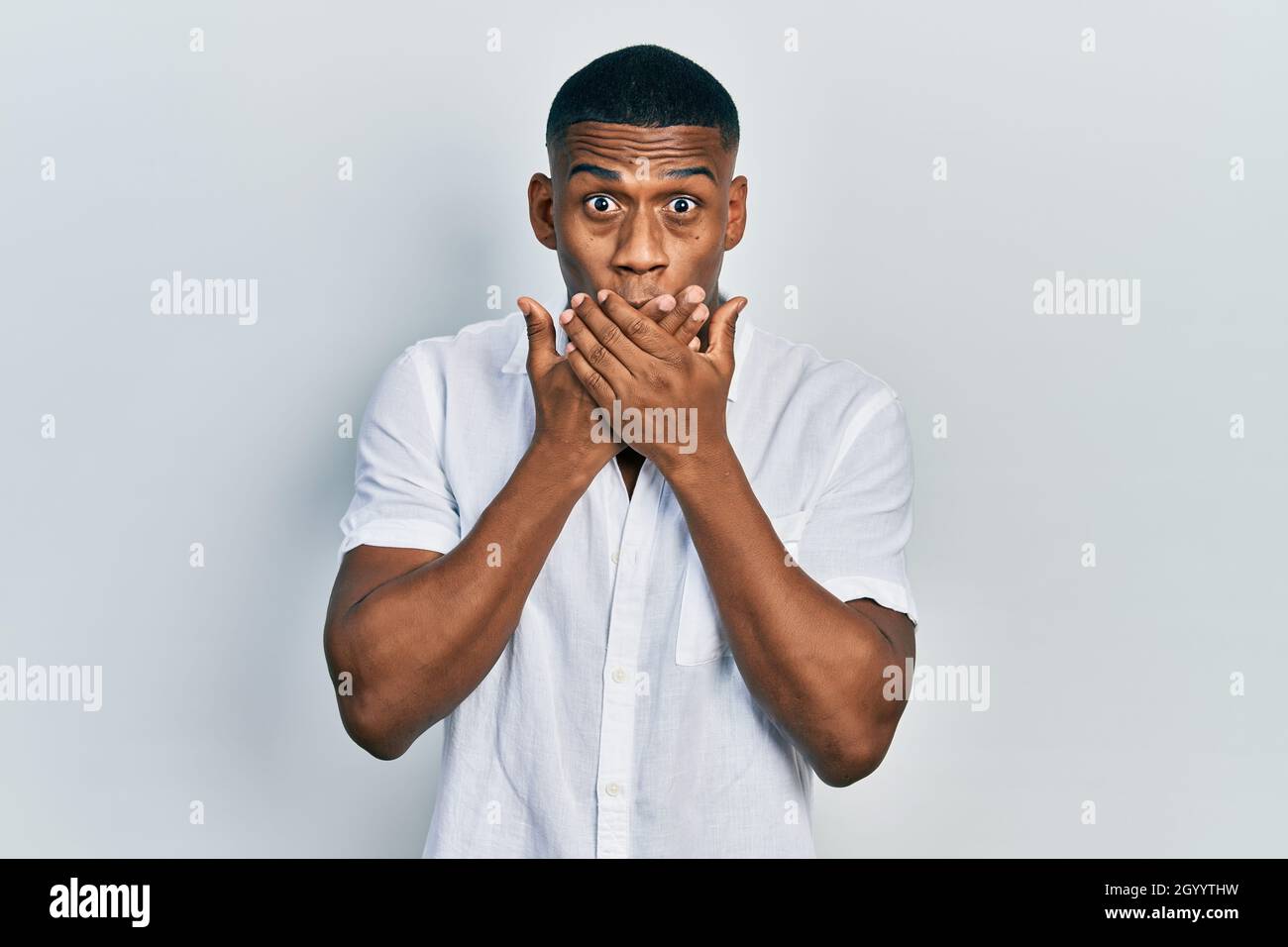 Young black man wearing casual white shirt shocked covering mouth with ...