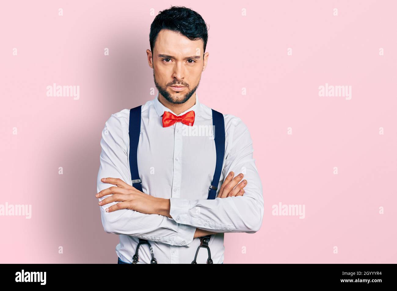 Hispanic man with beard wearing hipster look with bow tie and suspenders skeptic and nervous, disapproving expression on face with crossed arms. negat Stock Photo
