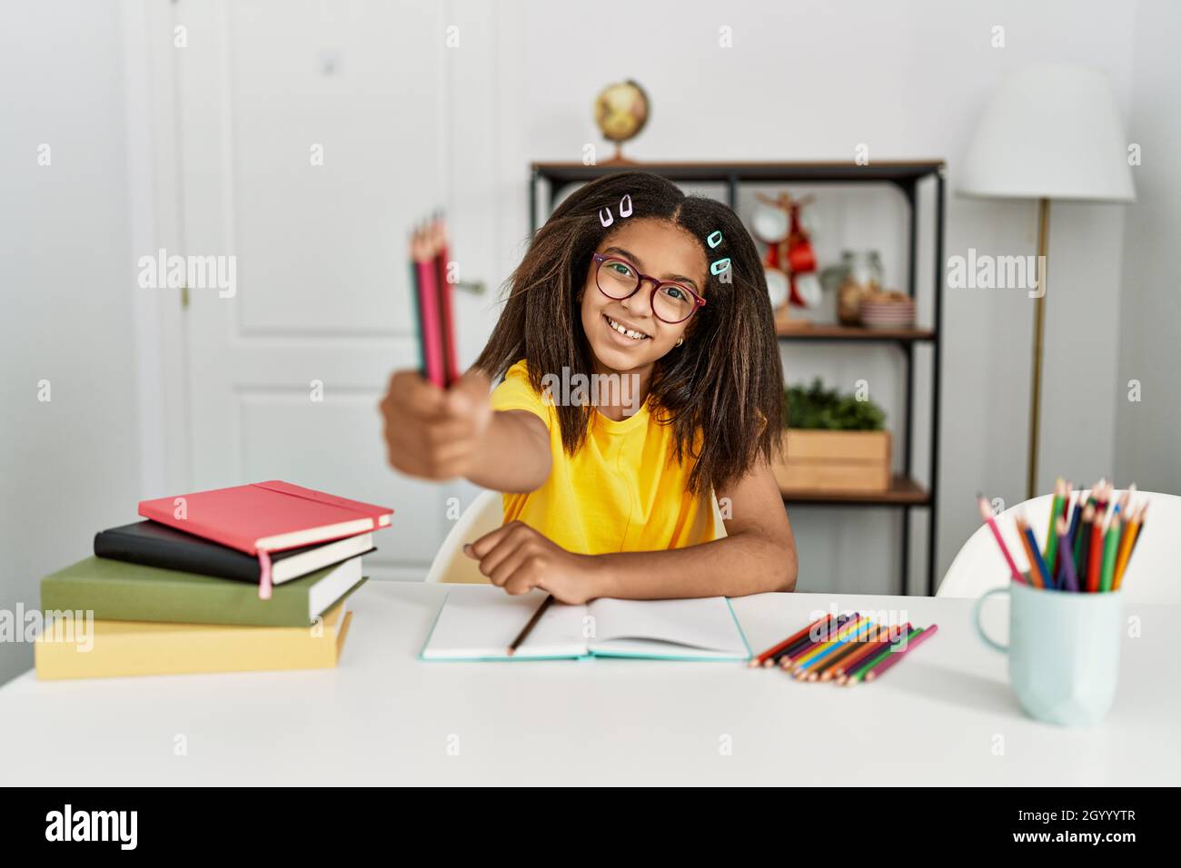African american girl doing school homework holding pencils at home ...