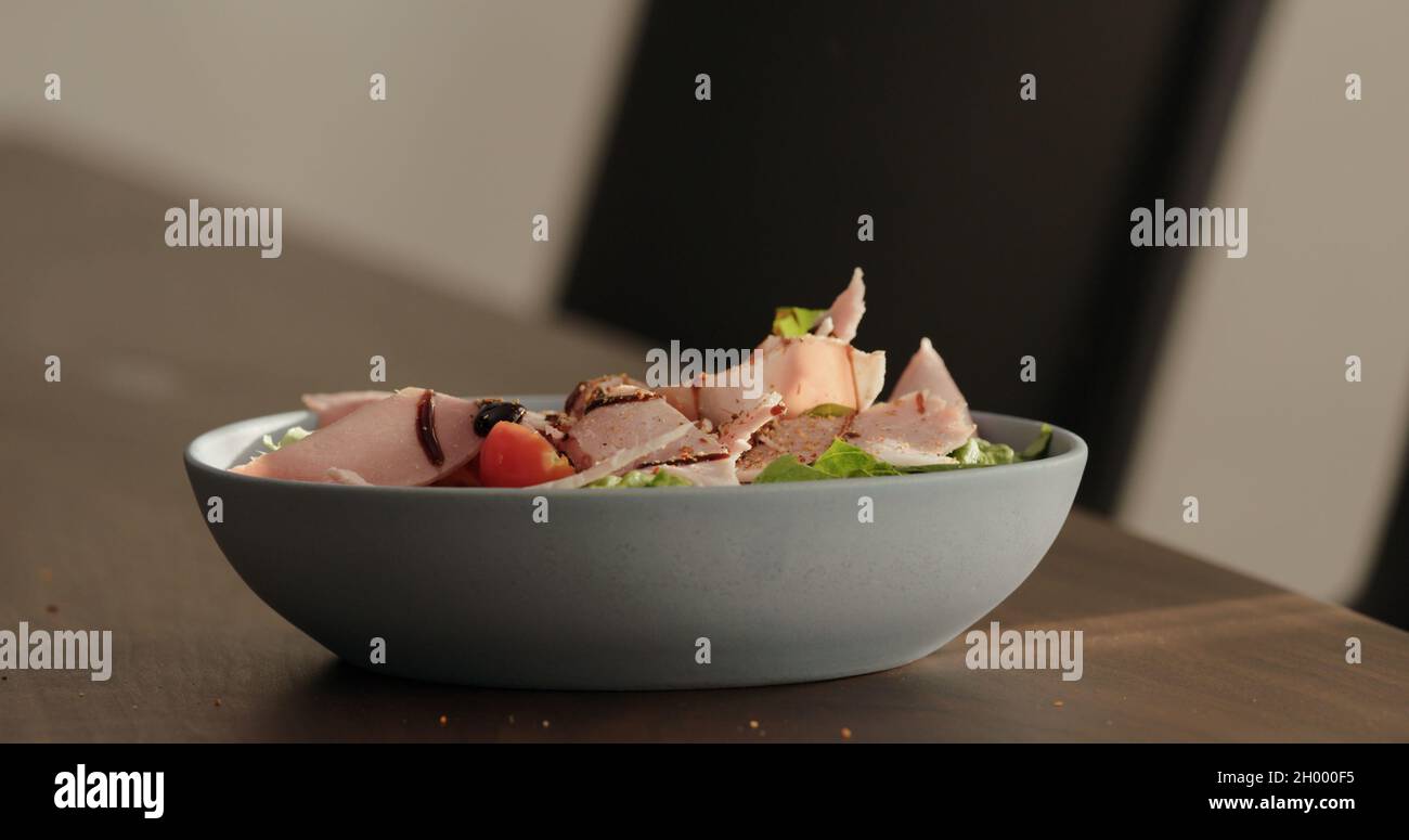 seasoning salad with prosciutto cotto and greens in blue bowl on walnut table, wide photo Stock Photo