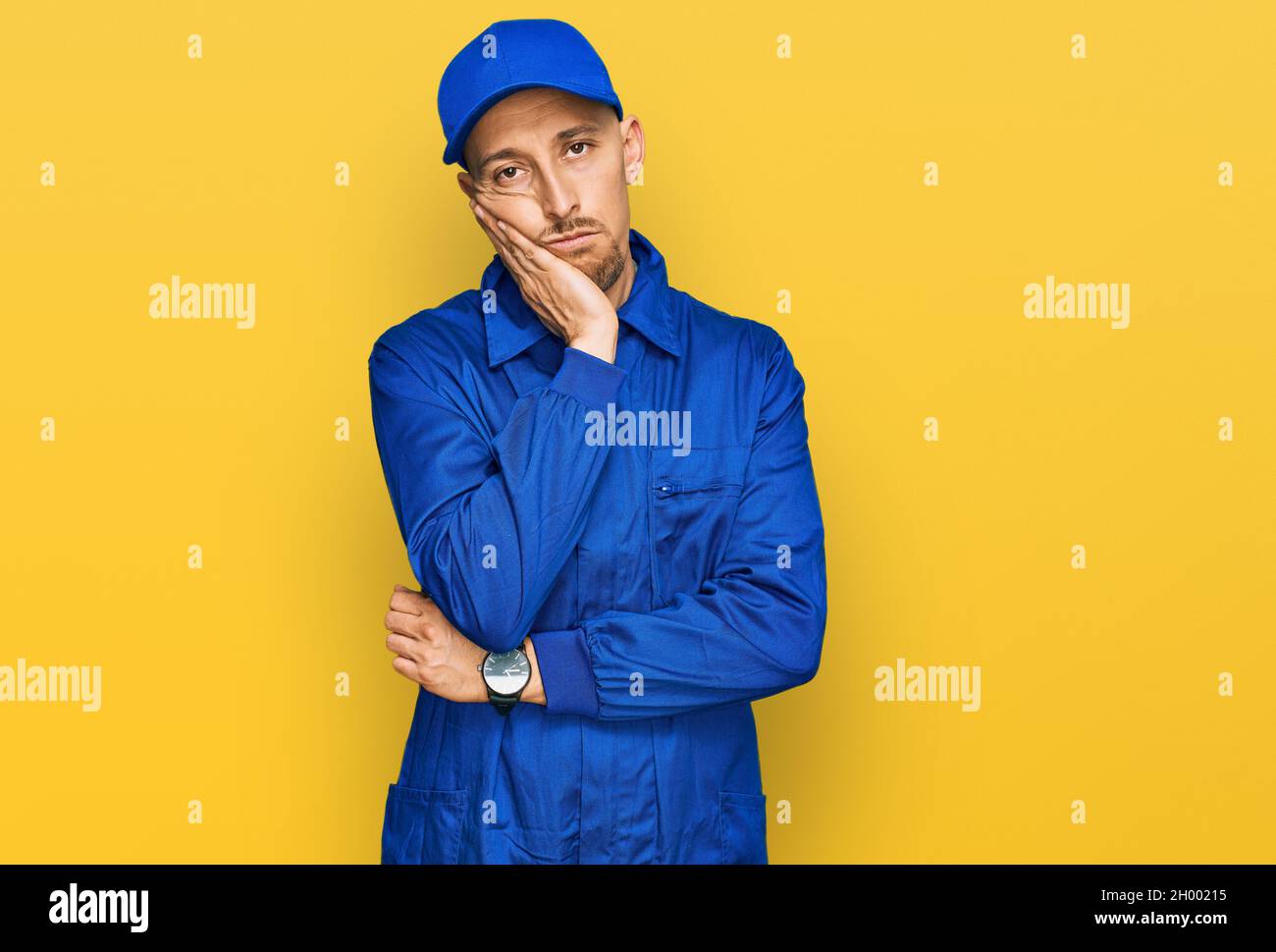 Bald man with beard wearing builder jumpsuit uniform thinking looking tired and bored with depression problems with crossed arms. Stock Photo
