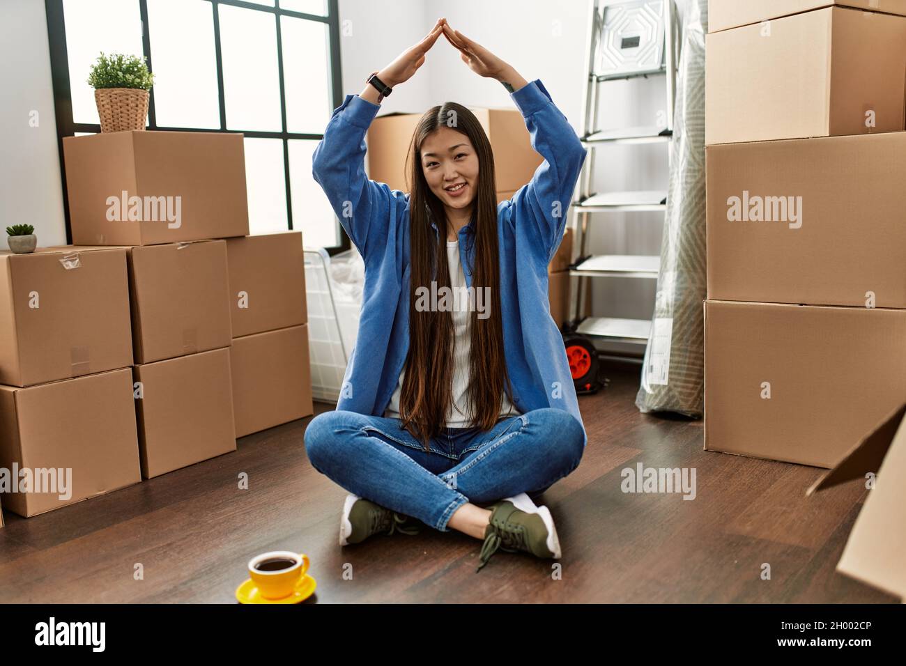 Young chinese girl smiling happy doing house gesture with hands raised ...
