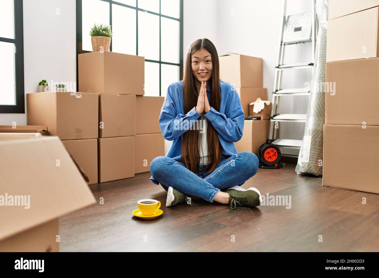Young chinese girl sitting on the floor at new home praying with hands ...