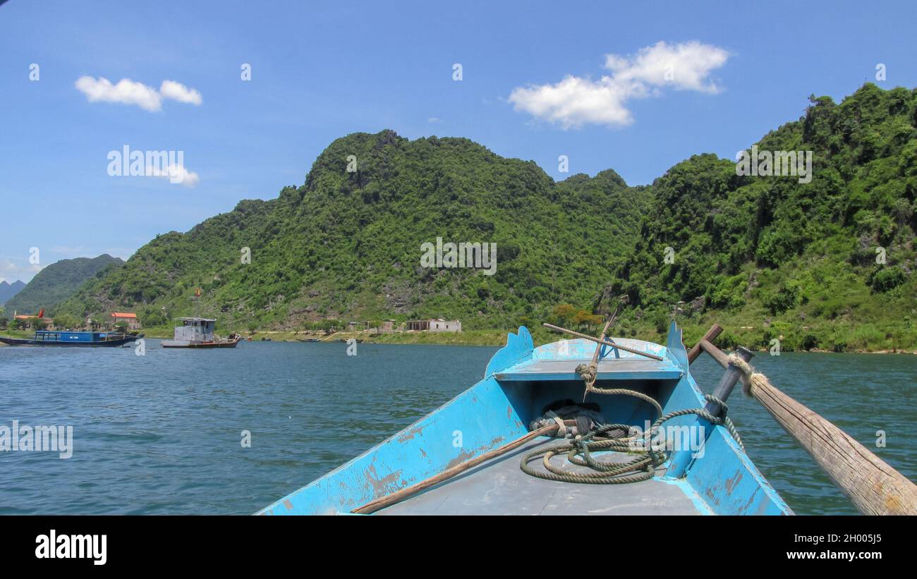 Looking at the blue river and high mountain from the bow of a small wooden boat in Phong Nha - Ke Bang National Park, Quang Binh Province, Vietnam Stock Photo