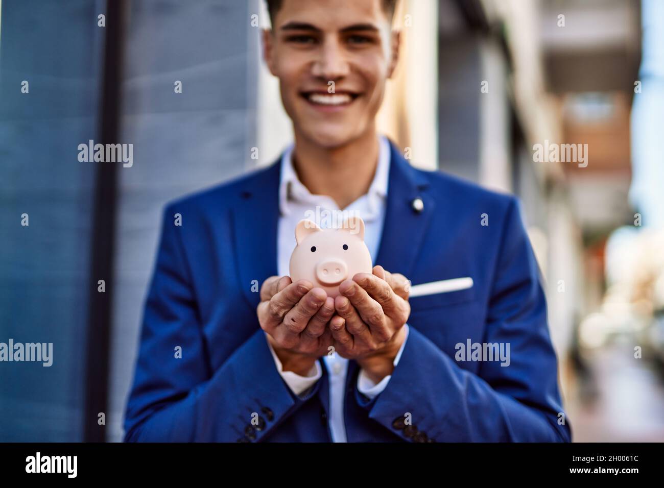 Young man wearing suit holding piggy bank at street Stock Photo - Alamy