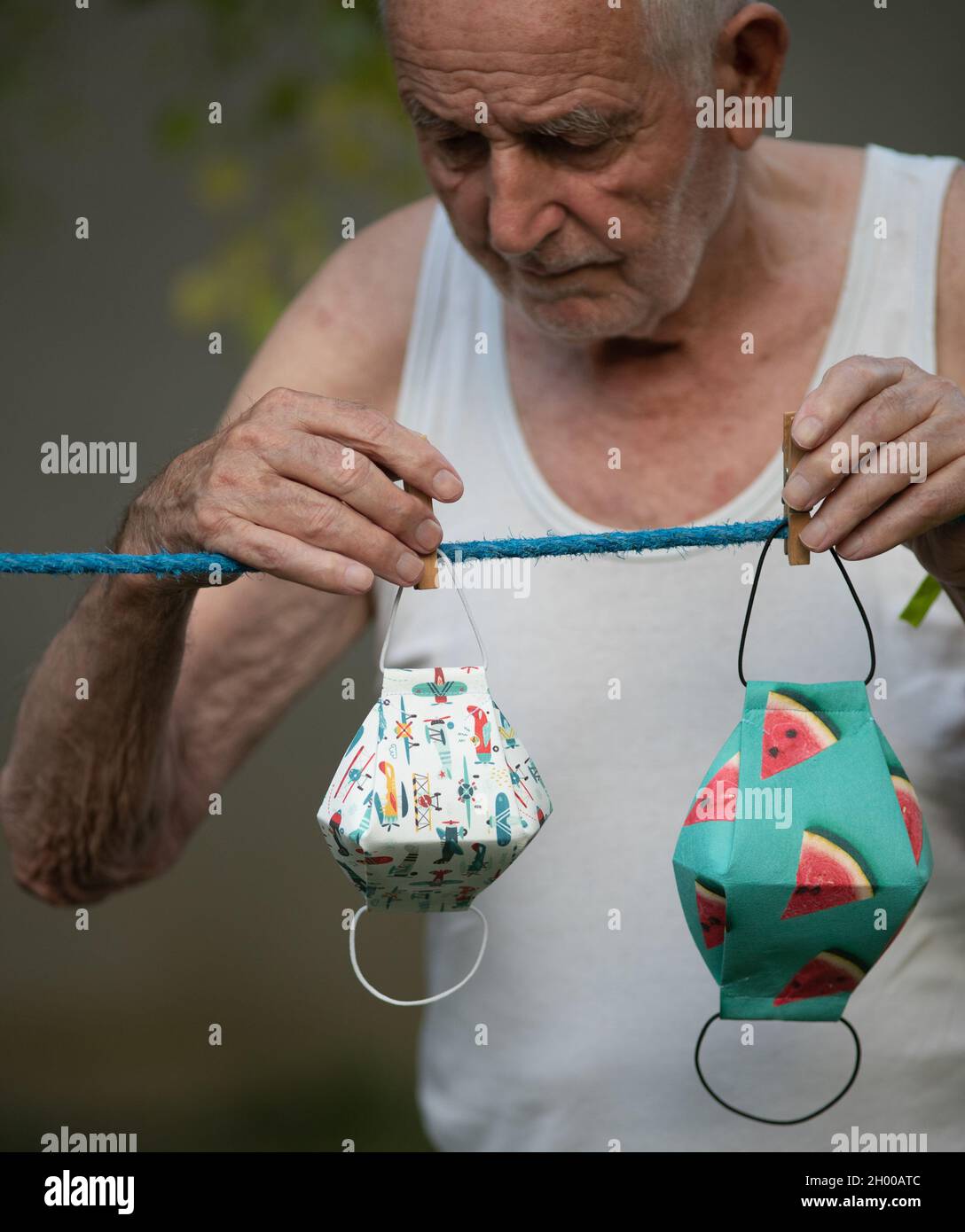 Senior man washing and drying safety cloth masks on hanger in garden during quarantine. Virus