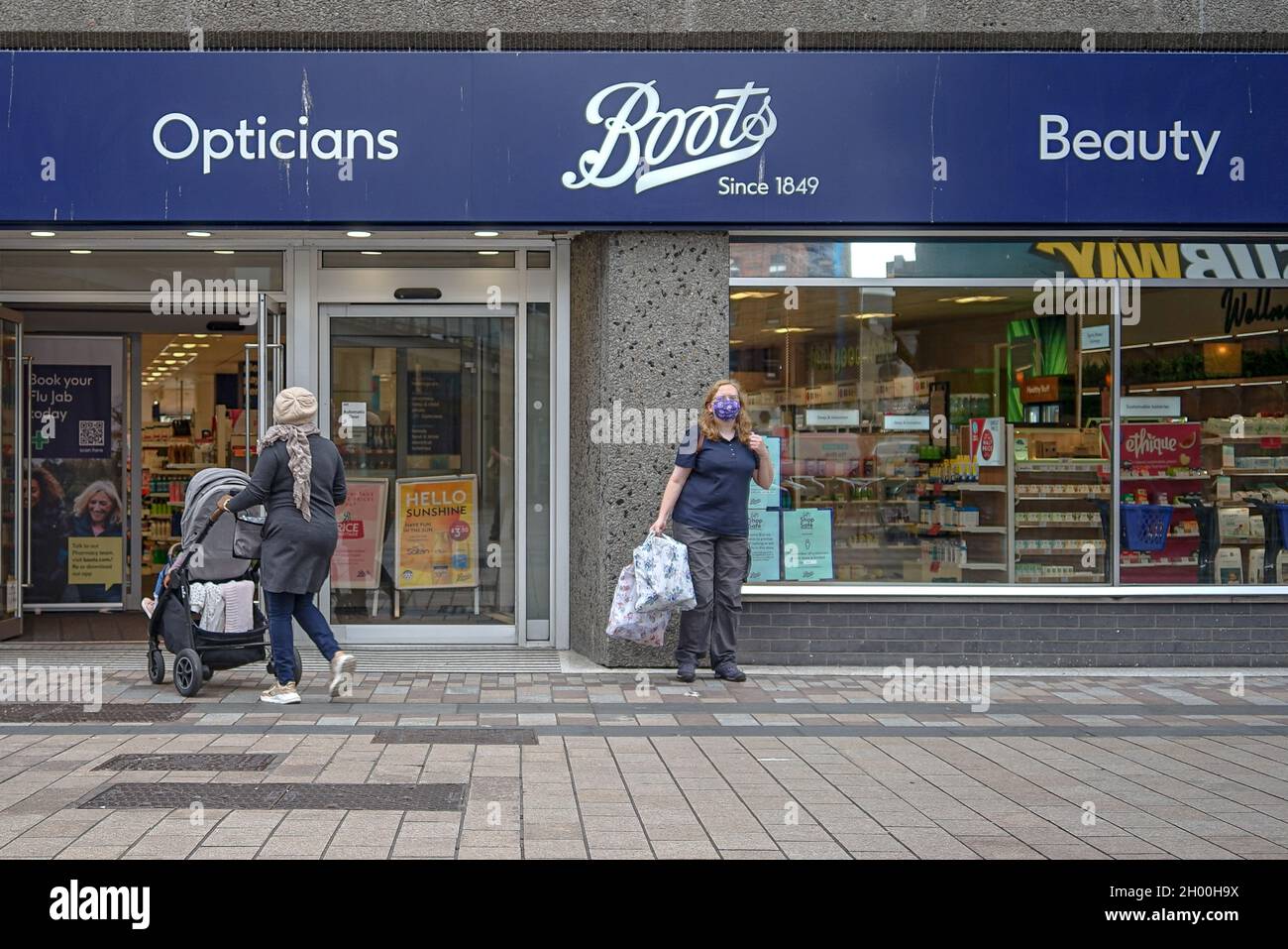 Masked pedestrians stand outside Boots Pharmacy on Fountain Lane in