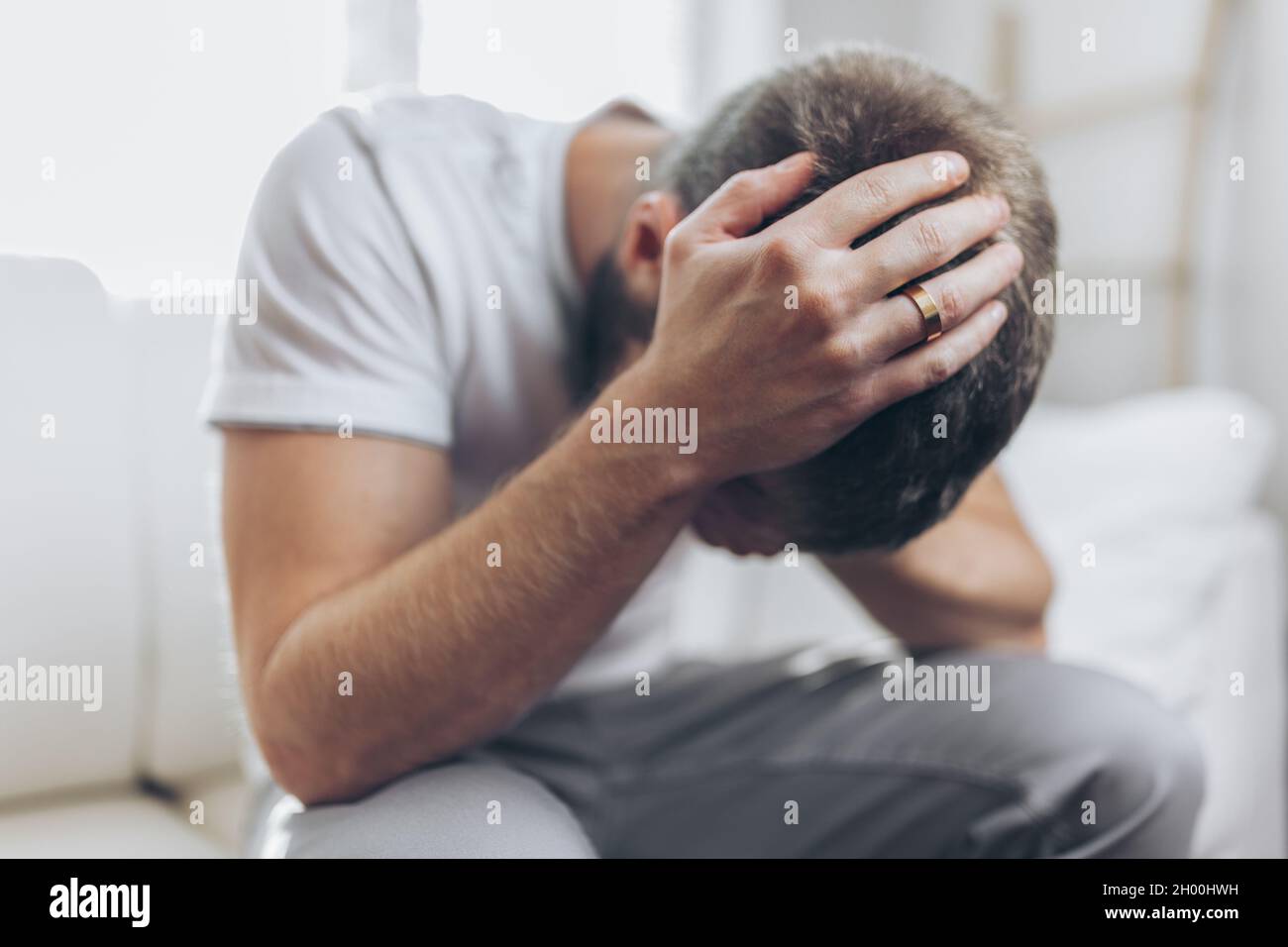 Heartbroken man at home holding a wedding ring Stock Photo
