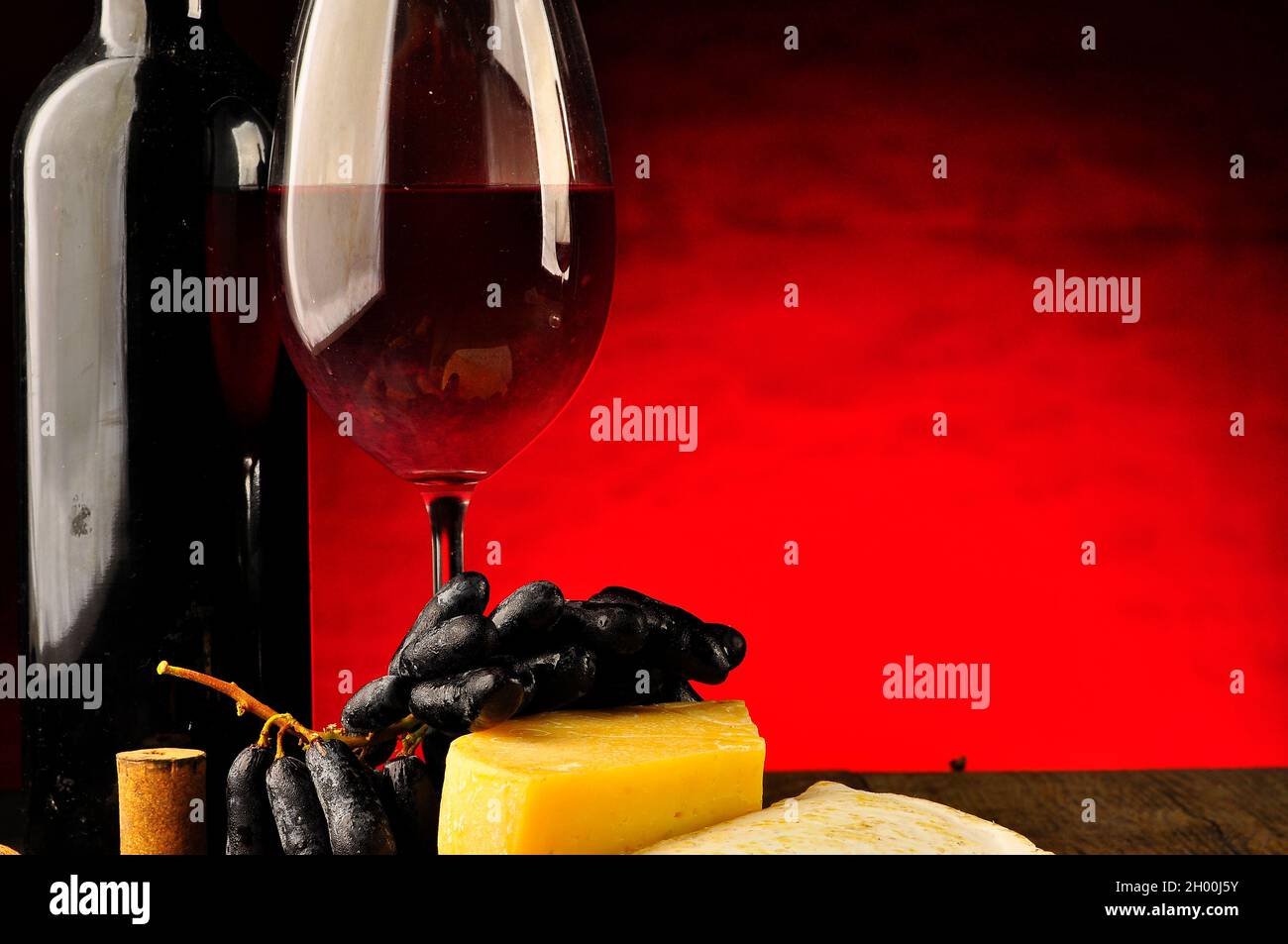 Glass and bottle of wine with a table of mixed cheese nearby Stock