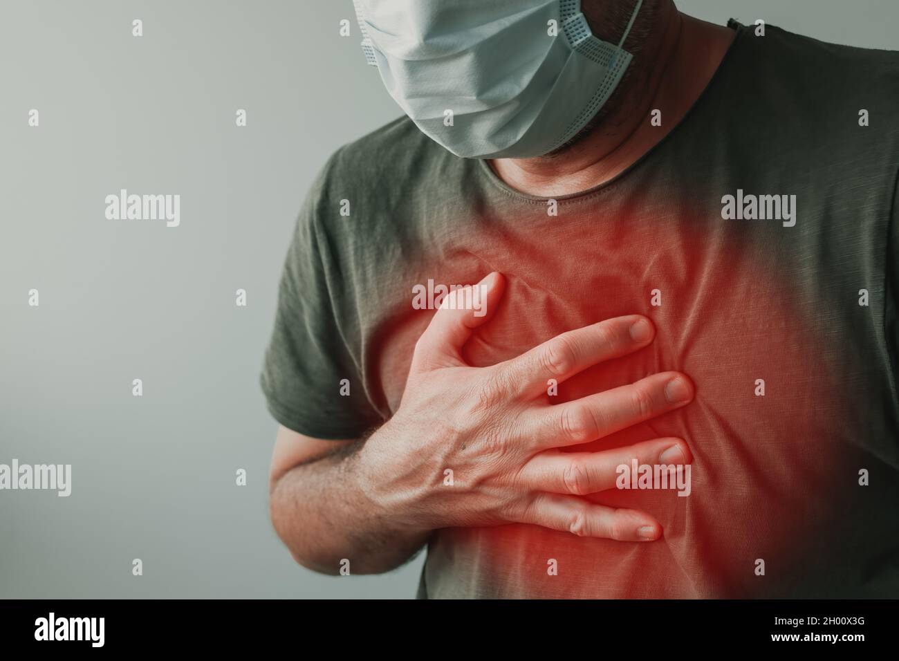 Covid-19 chest pain as infection symptom, man with respiratory mask holding a hand at his chest Stock Photo
