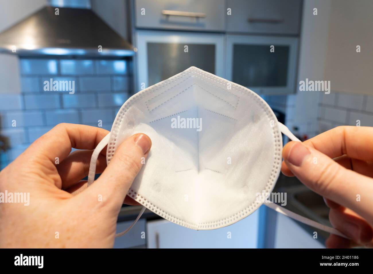 A man holding a face mask about to put it over his face at home for Covid-19 Coronavirus, seen from his POV (point of view). England Stock Photo