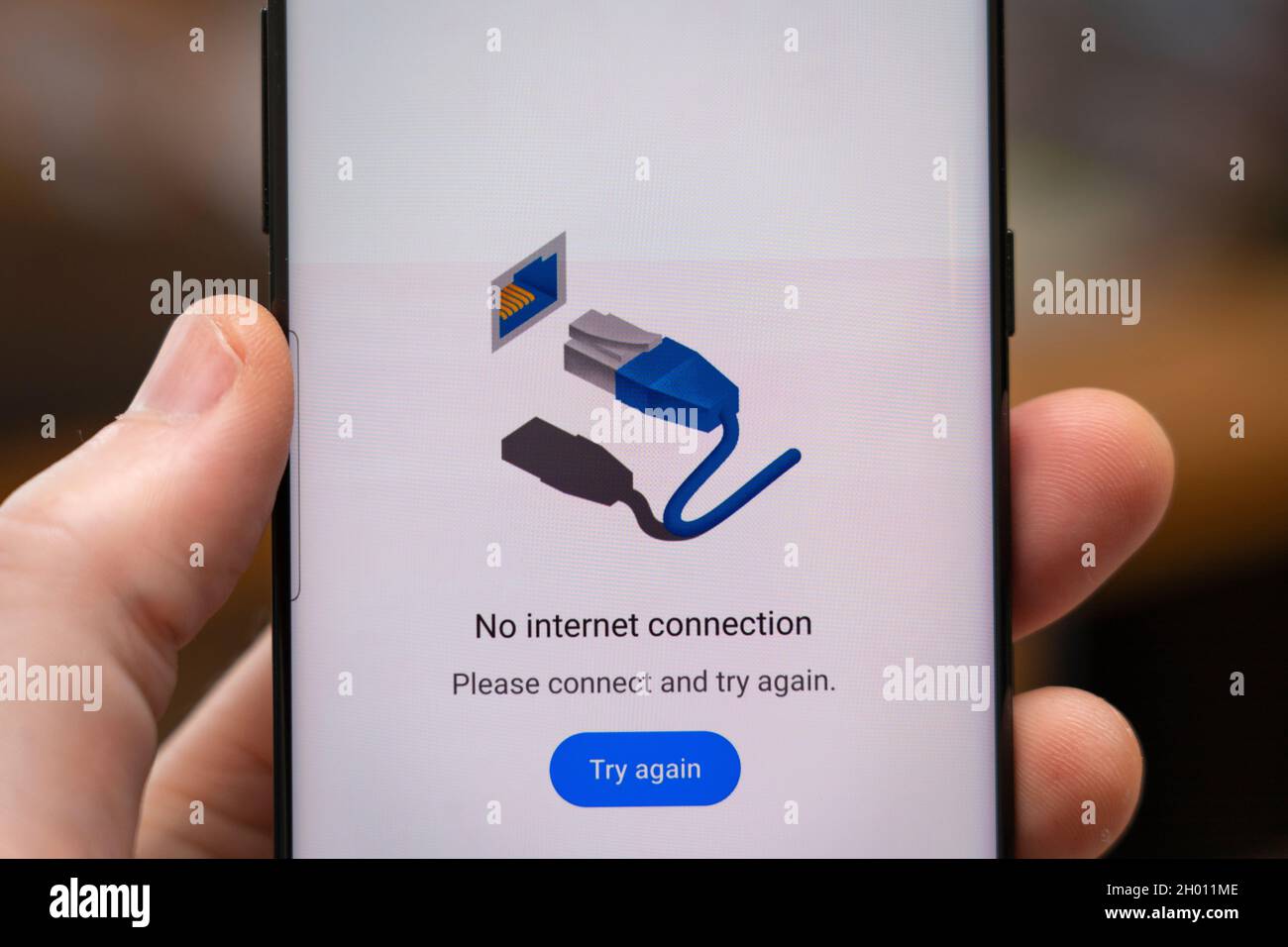 A man's hand holding a phone with a web page on a smartphone screen saying 'No internet connection' Stock Photo