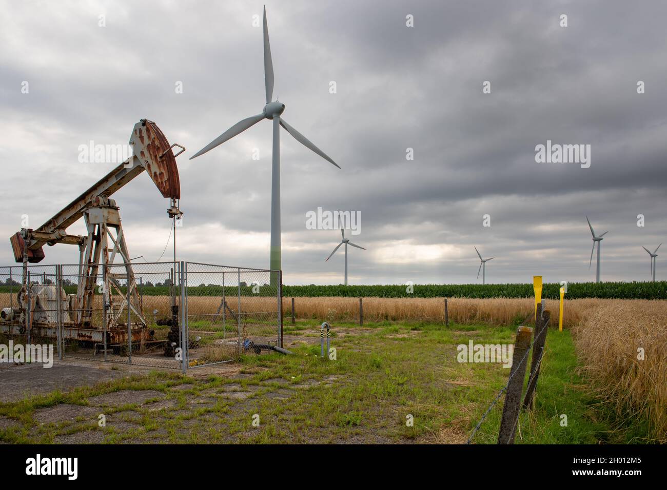 Old rusty oil hauling machines in front of modern wind turbines symbolizing energy transition at the face of climate change Stock Photo