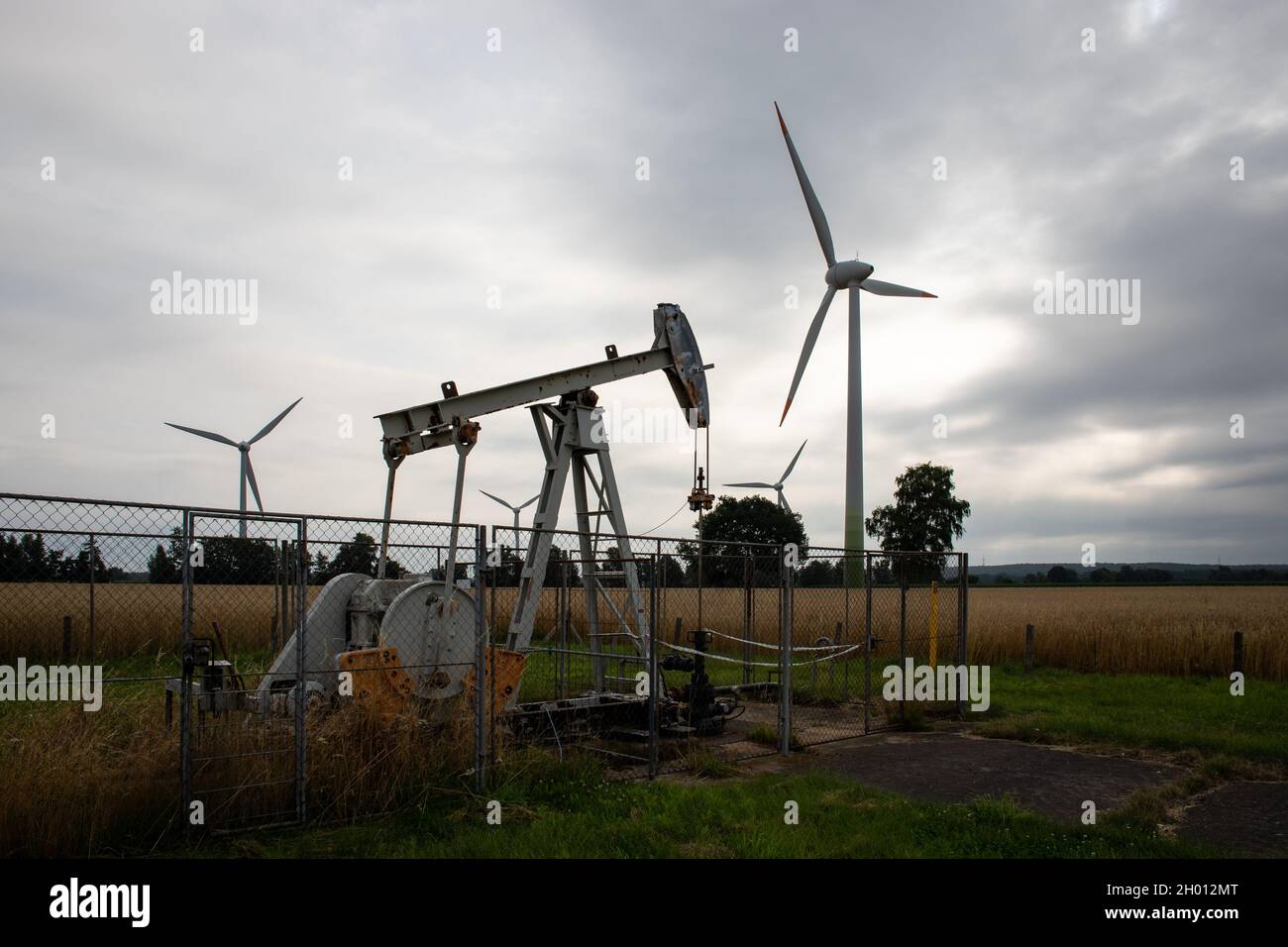 Old rusty oil hauling machines in front of modern wind turbines symbolizing energy transition at the face of climate change Stock Photo