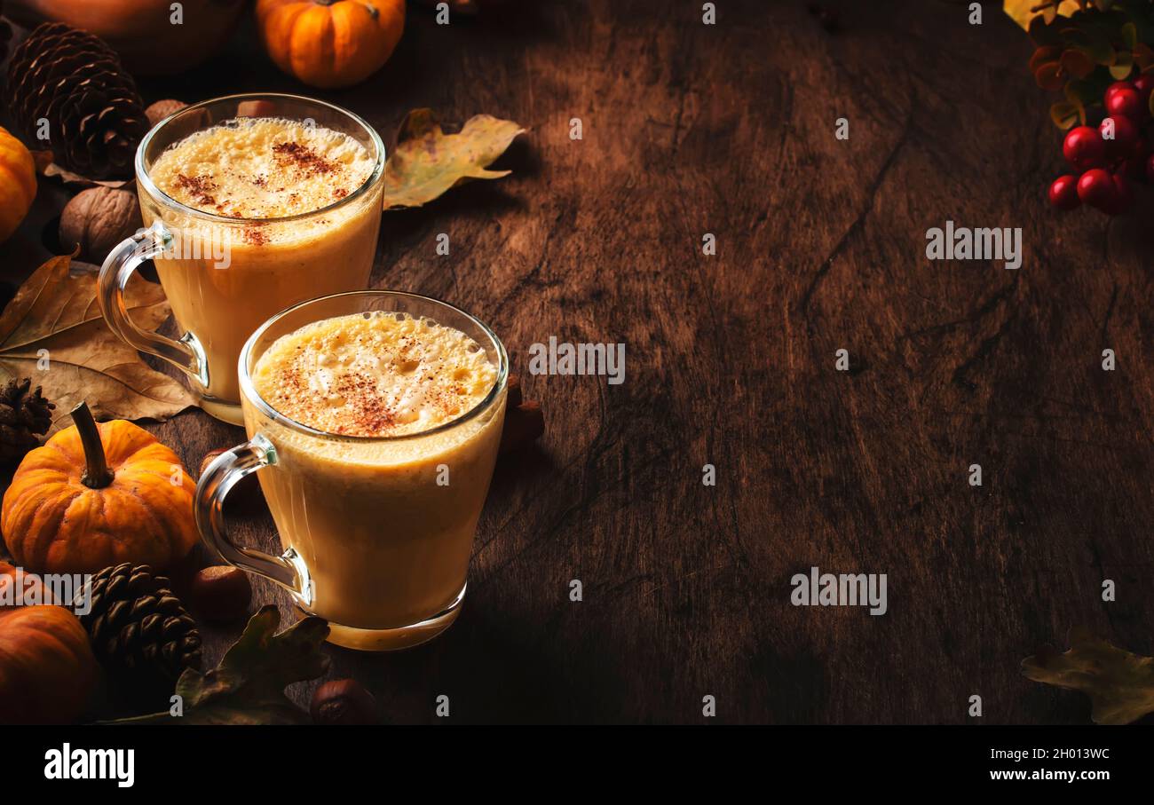 Pumpkin butter latte or coffee, keto drink on wooden table with fallen leaves, small pumpkins, pine cones and nuts. Autumn and winter hot drink and be Stock Photo