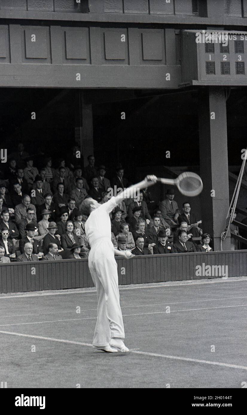 1930s, historical, a male tennis player wearing long trousers and a woollen sweatear, serving on a grass court at the famous Wimbledon tennis championships, owned and run by the All England Lawn Tennis & Croquet Club, founded in 1868. The first gentleman's tennis championships were held in 1877, when the service motion was underarm. Stock Photo
