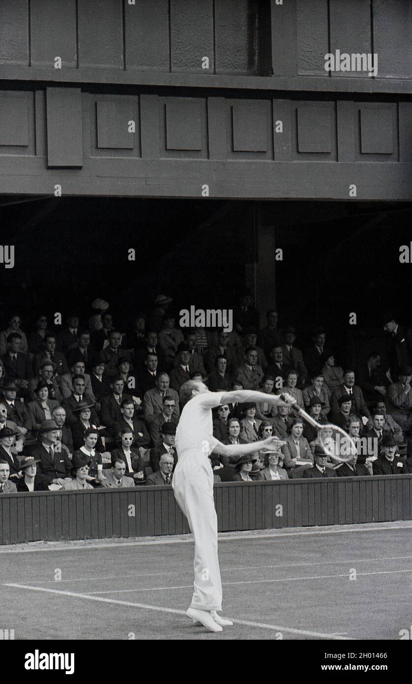 1930s, historical, a male tennis player wearing long trousers and a woollen sweatear, serving on a grass court at the famous Wimbledon tennis championships, owned and run by the All England Lawn Tennis & Croquet Club, founded in 1868. The first gentleman's tennis championships were held in 1877, when the service motion was underarm. Stock Photo