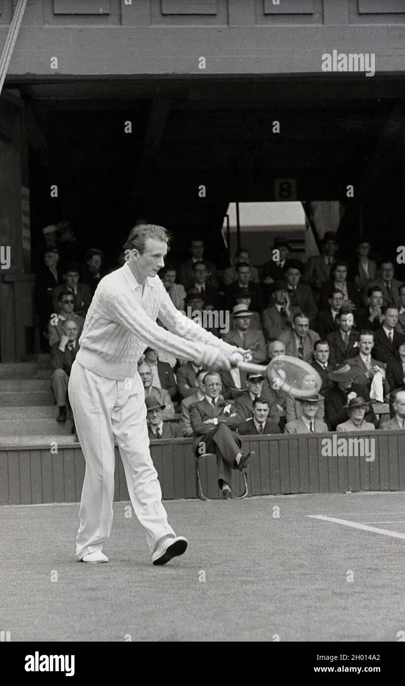 1930s, historical, a male tennis player wearing long trousers and a woollen sweatear, serving on a grass court at the famous Wimbledon tennis championships, owned and run by the All England Lawn Tennis & Croquet Club, founded in 1868. The first gentleman's tennis championships were held in 1877, when the service motion was underarm. Stock Photo