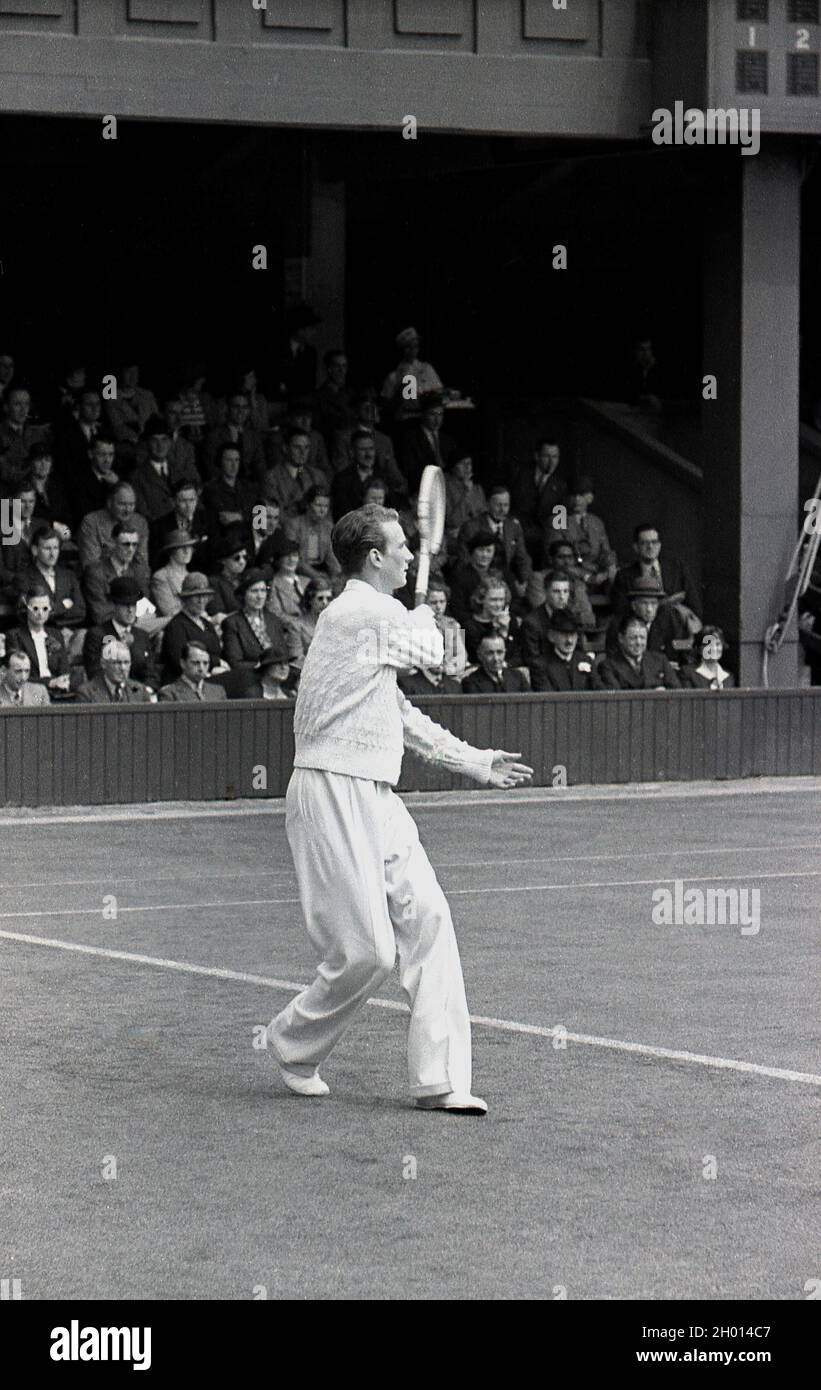 1930s, historical, a male tennis player wearing long trousers and a woollen sweatear, serving on a grass court at the famous Wimbledon tennis championships, owned and run by the All England Lawn Tennis & Croquet Club, founded in 1868. The first gentleman's tennis championships were held a few years later in 1877. Stock Photo
