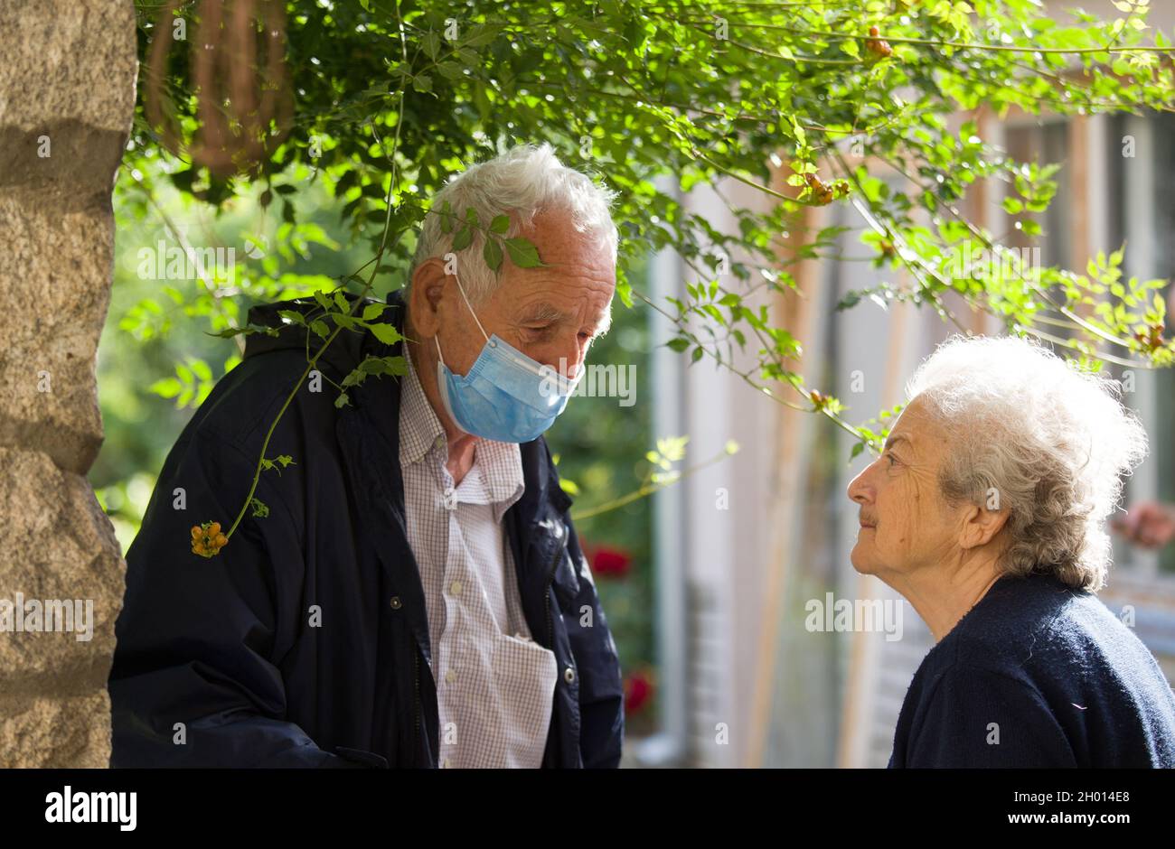 Senior man with mask talking to old woman in neighborhood after pandemic. Safety and protection measures for elderly people Stock Photo