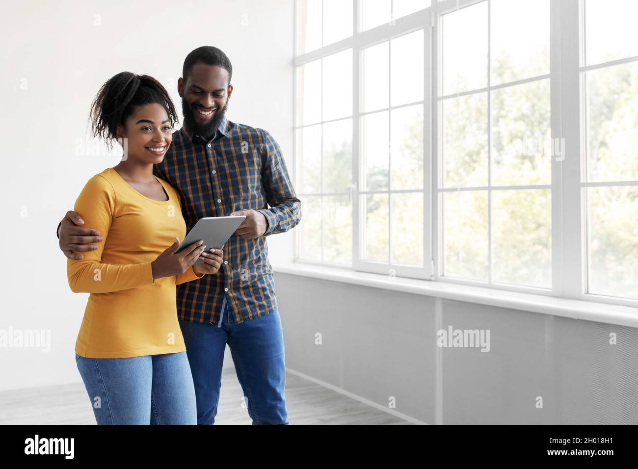 Smiling young african american husband and wife looking in tablet ...