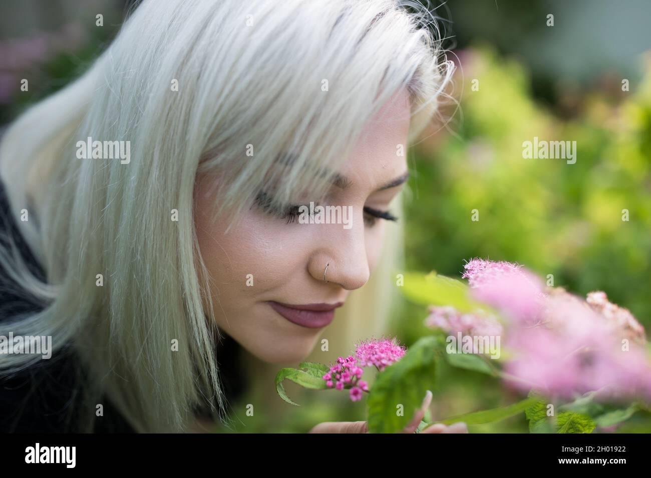 Portrait of pretty blond teenage girl smelling pink flowers in garden ...