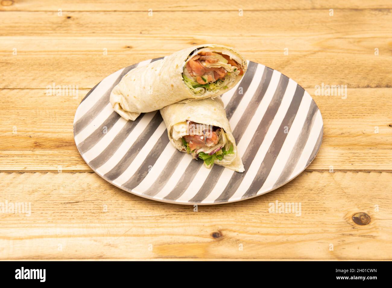 wrap stuffed with smoked Norwegian salmon with cheese and lettuce on a grated plate Stock Photo
