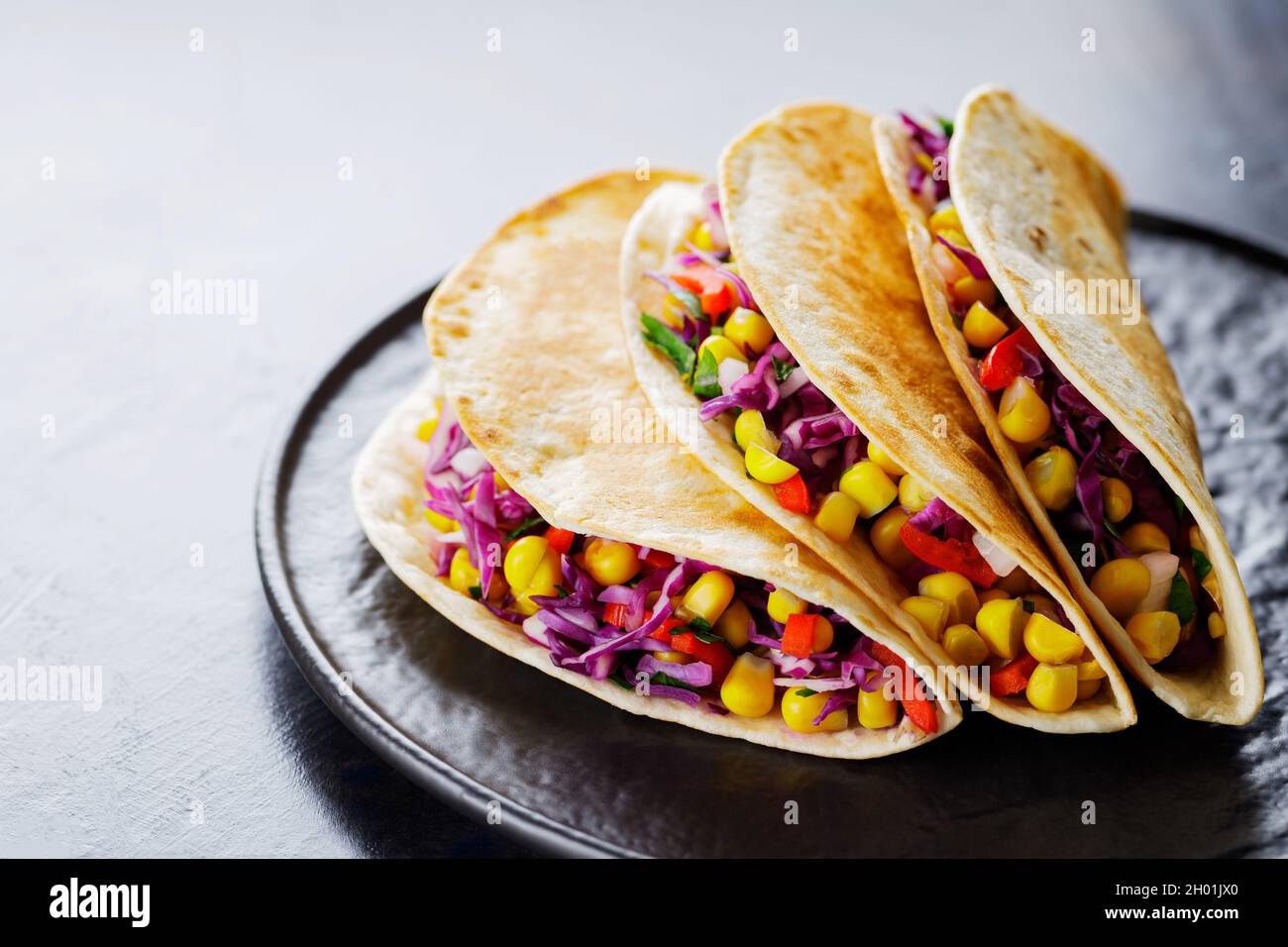 Vegetarian tacos with various vegetables, guacamole and lime on dark background. Tacos with sweet corn, purple cabbage and tomatoes on a black plate. Stock Photo