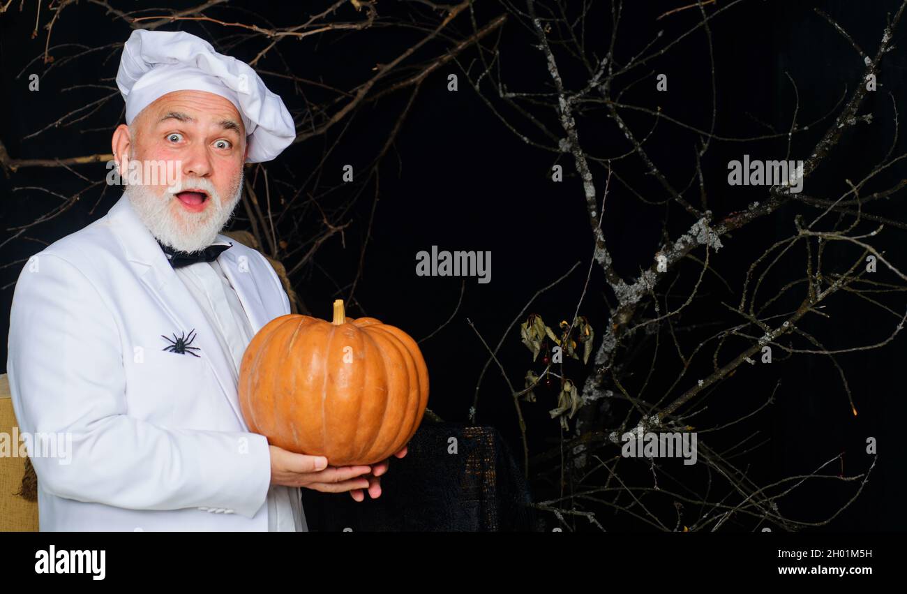 Male chef in uniform with pumpkin. Autumn recipes concept. Useful vegetables. Happy halloween. Bearded cook in chef hat with pumpkin. Stock Photo