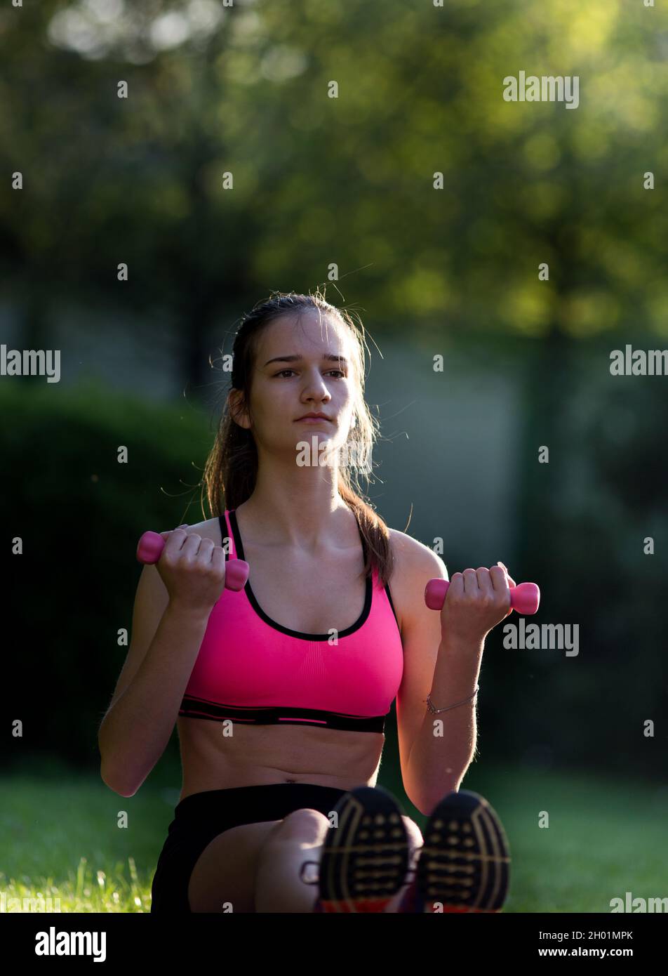 Fit teenage girl doing exercise with dumbbells on mat on grass in park un summer time. Healthy lifestyle concept Stock Photo