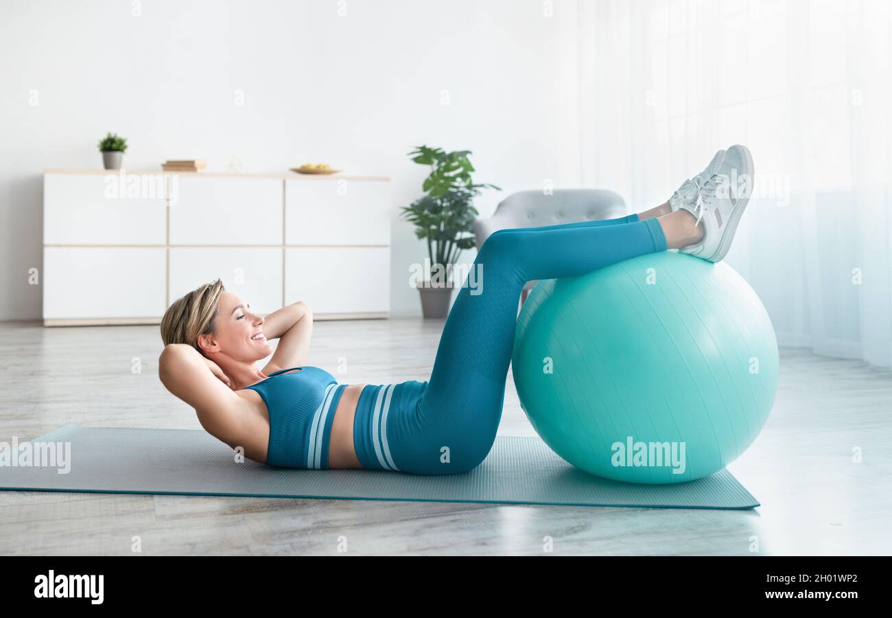 Smiling sporty woman doing abs sit-ups exercises holding legs on ...