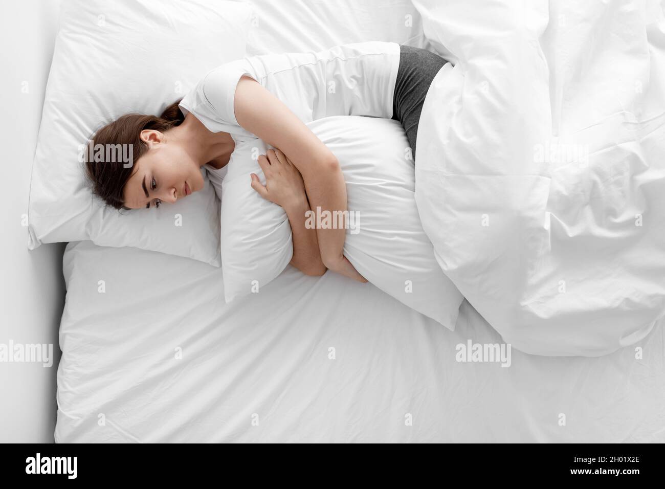 Despaired upset sad european millennial woman hugging pillow and lying