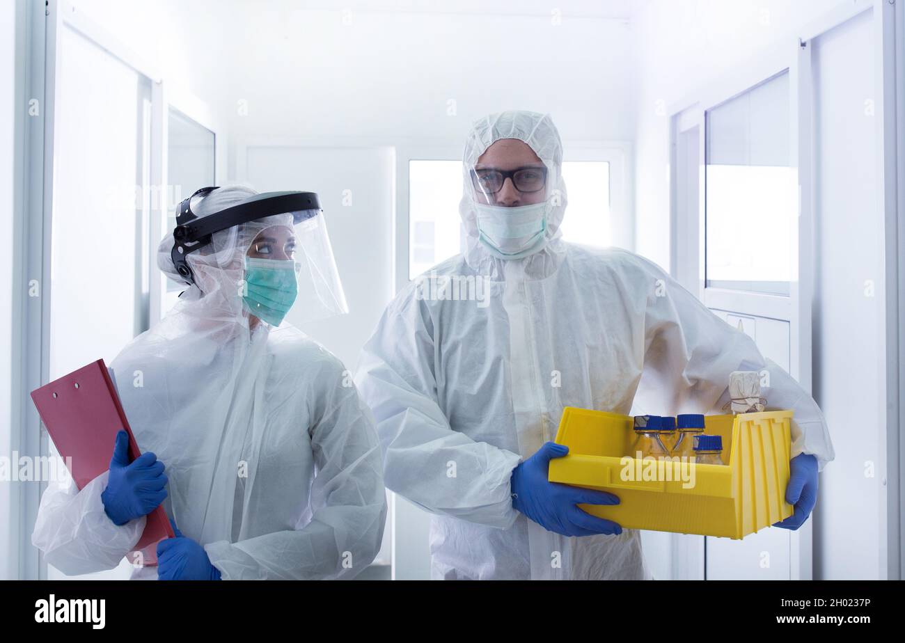 Two biologists in protective suits carrying samples in laboratory ...