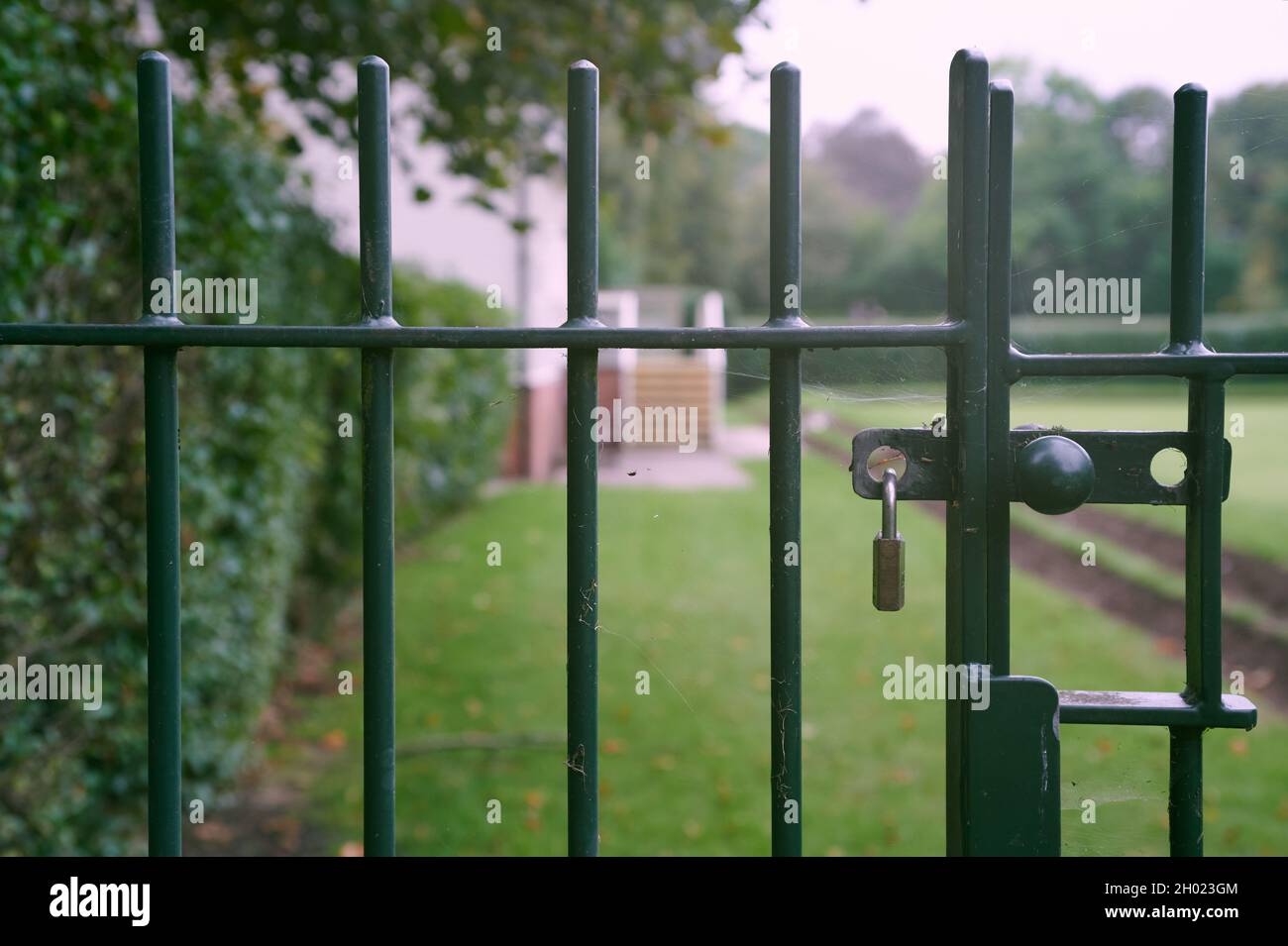 Padlocked closed green metal gate with out of focus park and lawn in background Stock Photo
