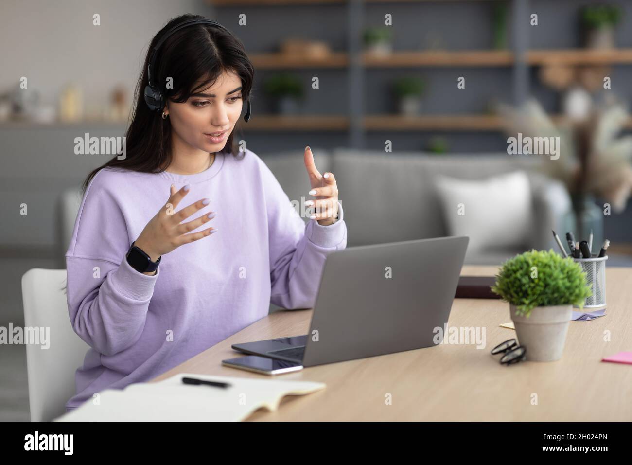 Portrait of focused woman in headphones looking at laptop screen and talking during webinar, consulting client, explaining lesson or business strategy Stock Photo