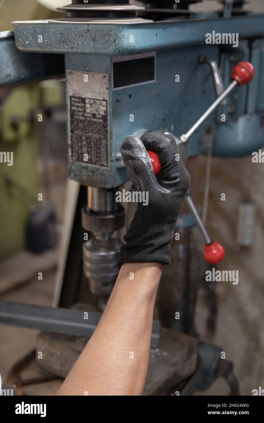 hand of a person wearing black protective gloves, holding the lever of a metal machine, working tools in factory, detail of object Stock Photo