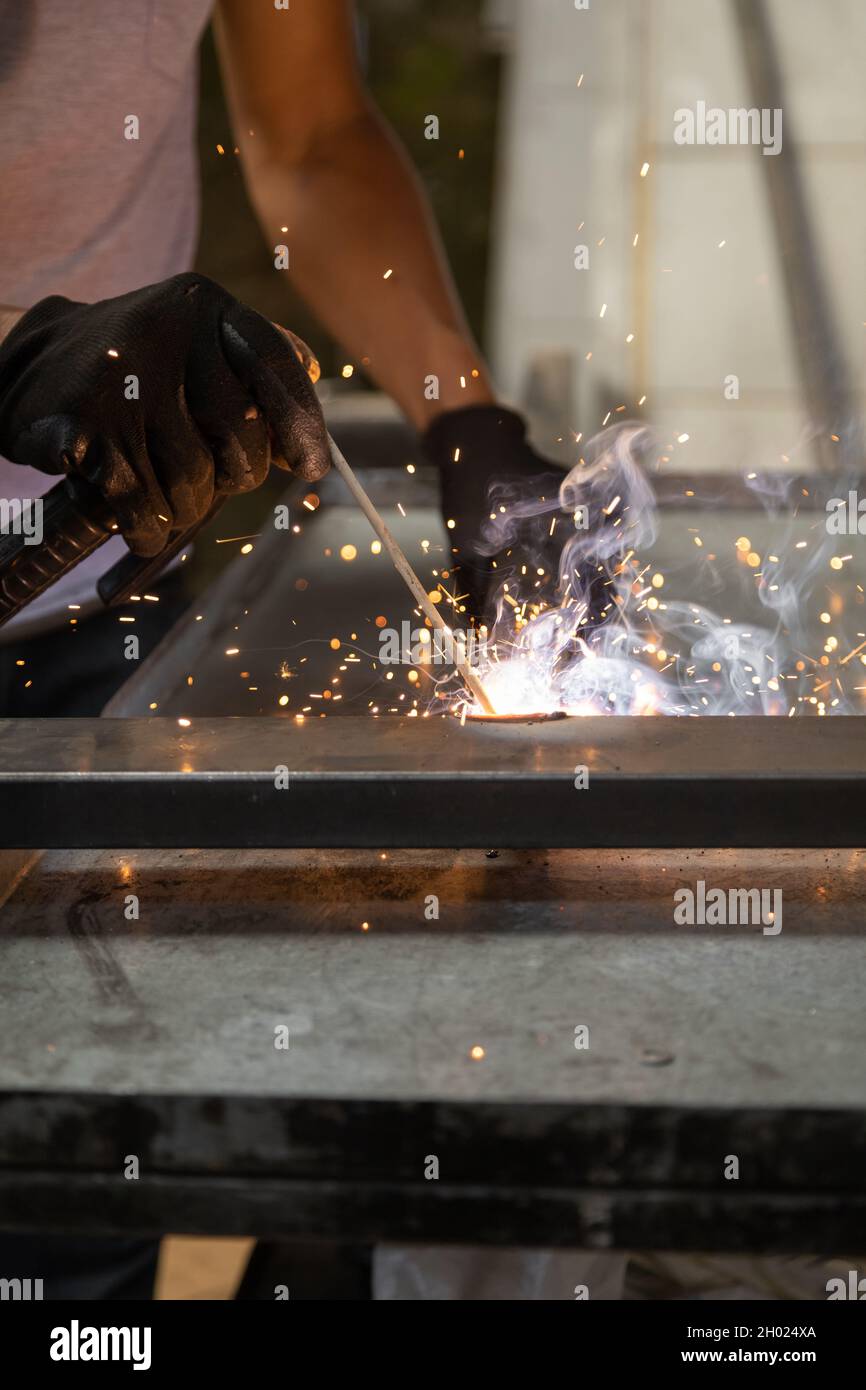 details of a person's hand wearing protective gloves while using a metal welding tool, sparks from the machine, manual work Stock Photo