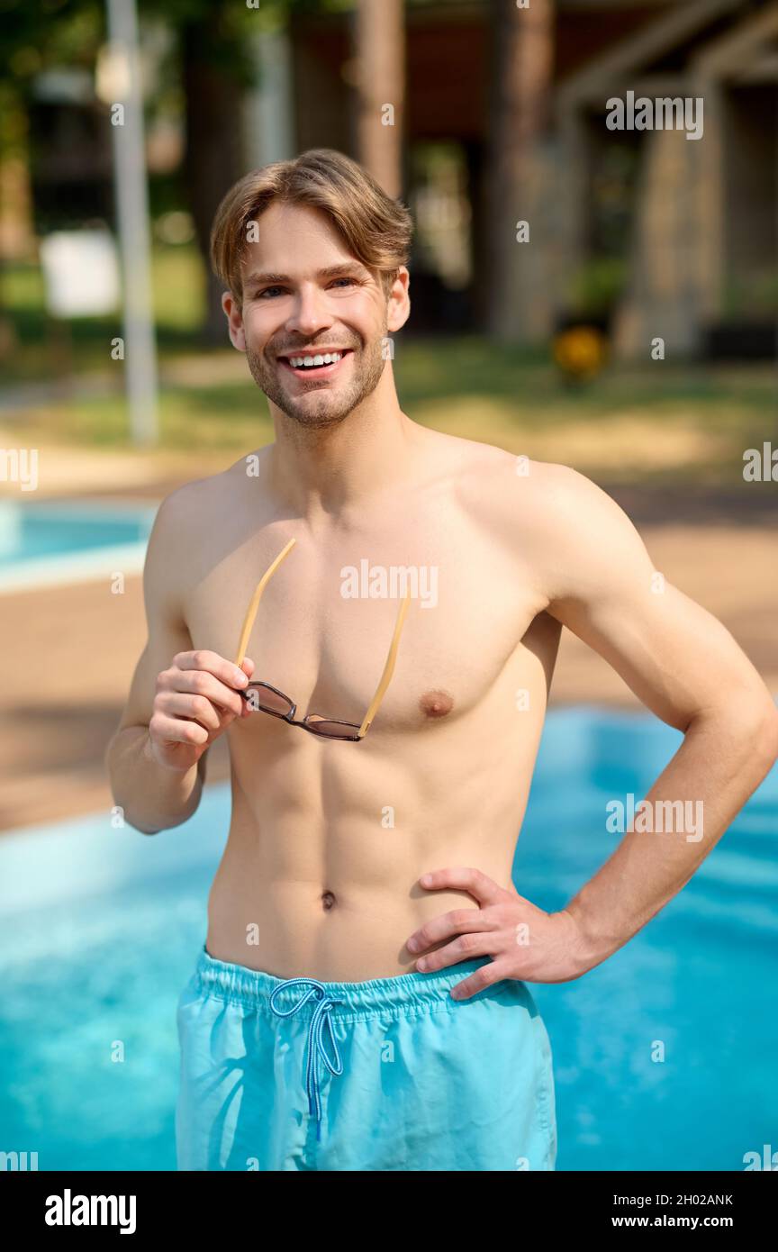 A handsome young man in blue shorts standing at the swimming pool Stock ...