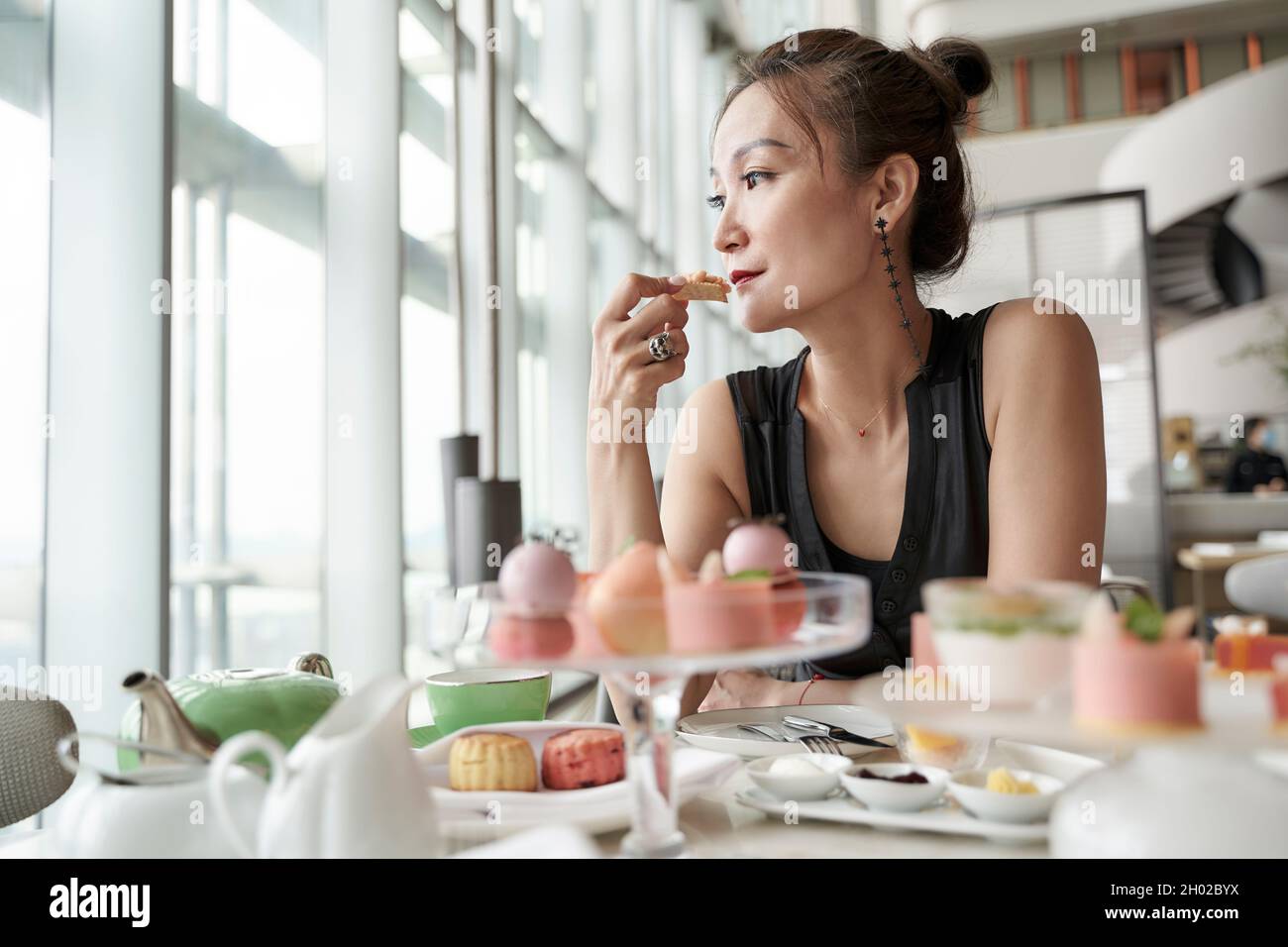 mature asian woman sitting at table eating dessert alone in hotel lobby coffee shop Stock Photo