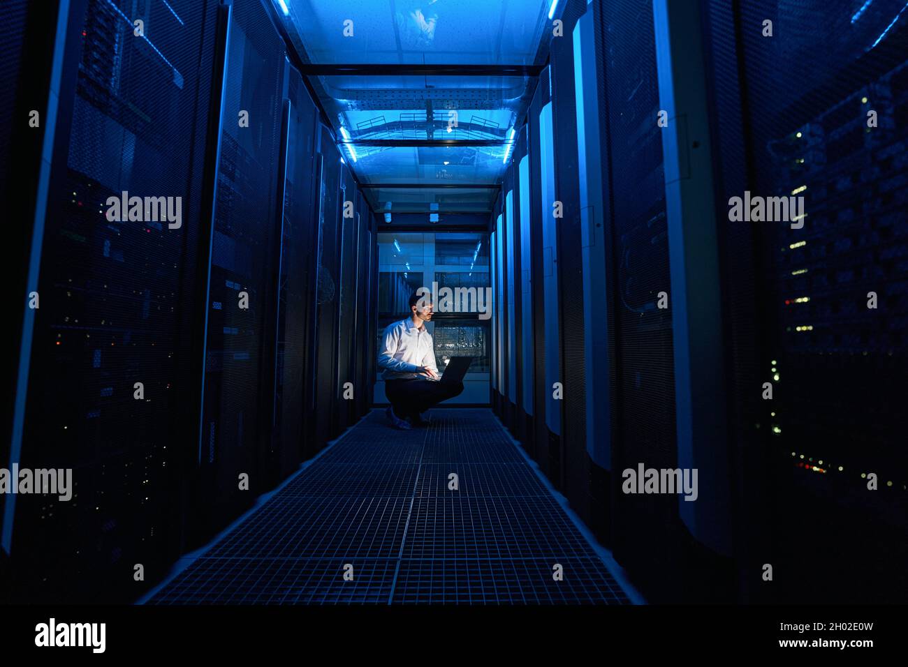 Technician looking at server cabinet while using laptop Stock Photo