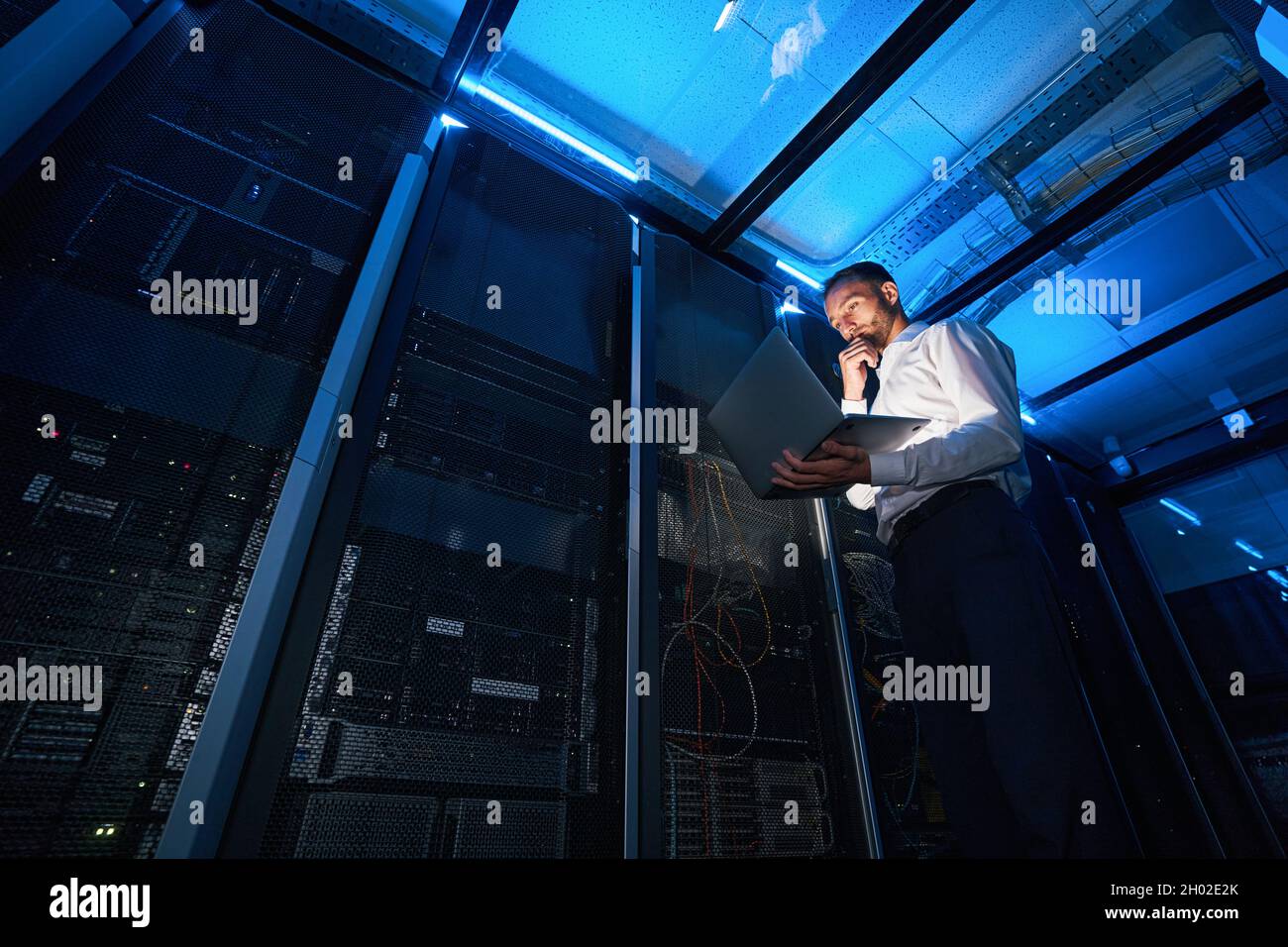 IT technician analyzing data from laptop in server room Stock Photo