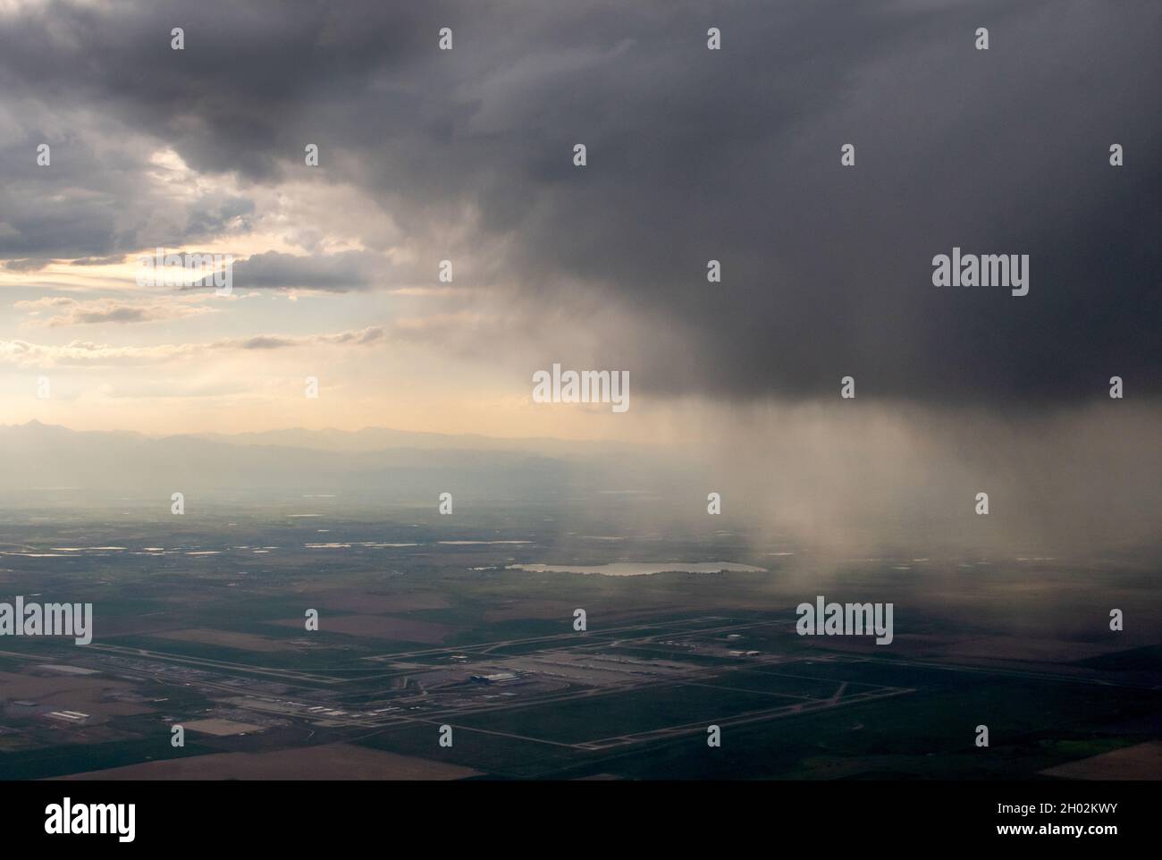 rain and storm clouds pour down over a city while viewed from the window of an airplane Stock Photo