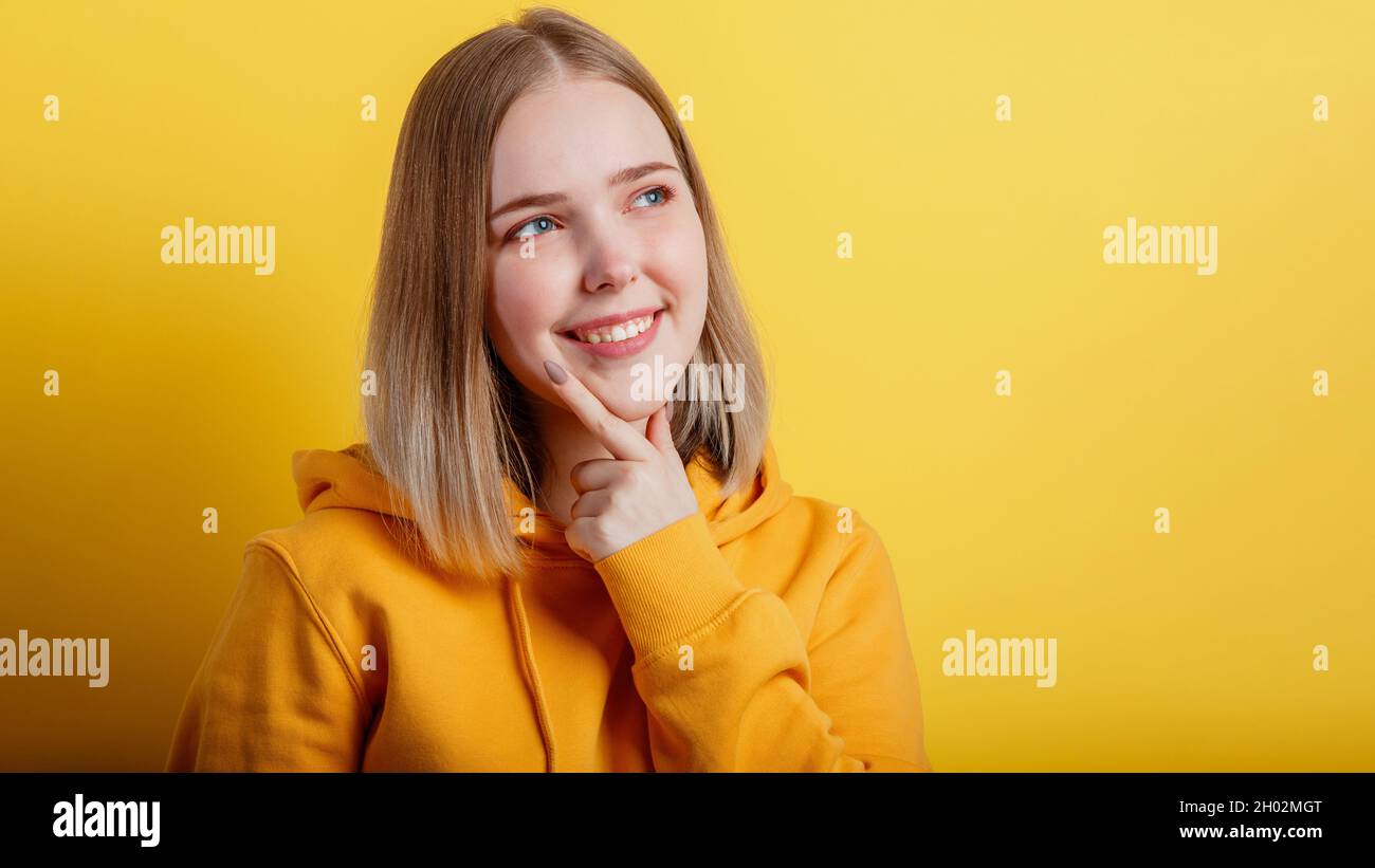 Happy smiling young woman think thought. Portrait of emotional teenage girl looking on empty space deep thinking about on color yellow background Stock Photo