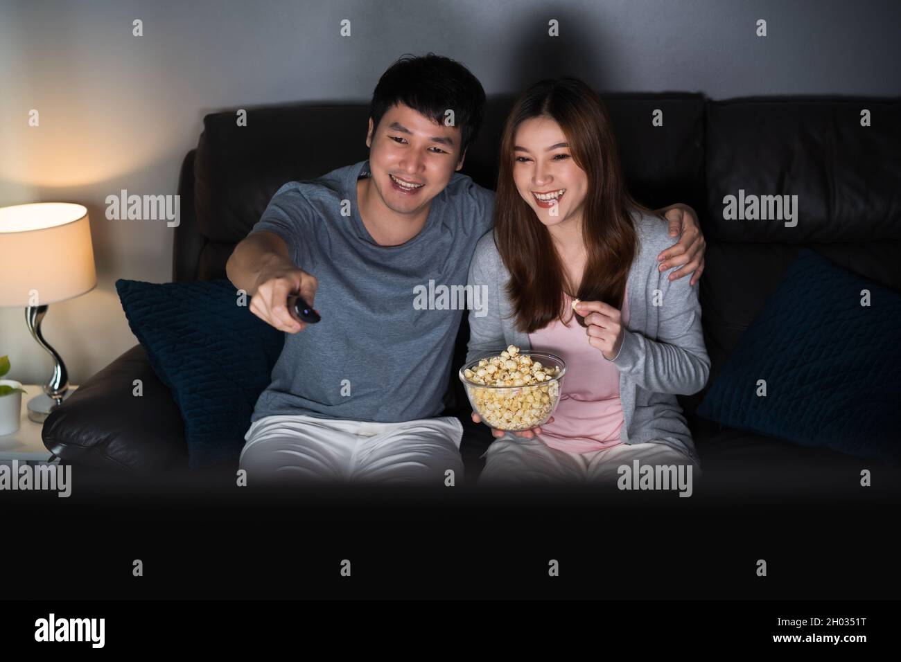 happy young couple watching TV on sofa at night Stock Photo