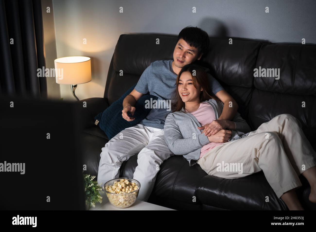 happy young couple watching TV on sofa at night Stock Photo