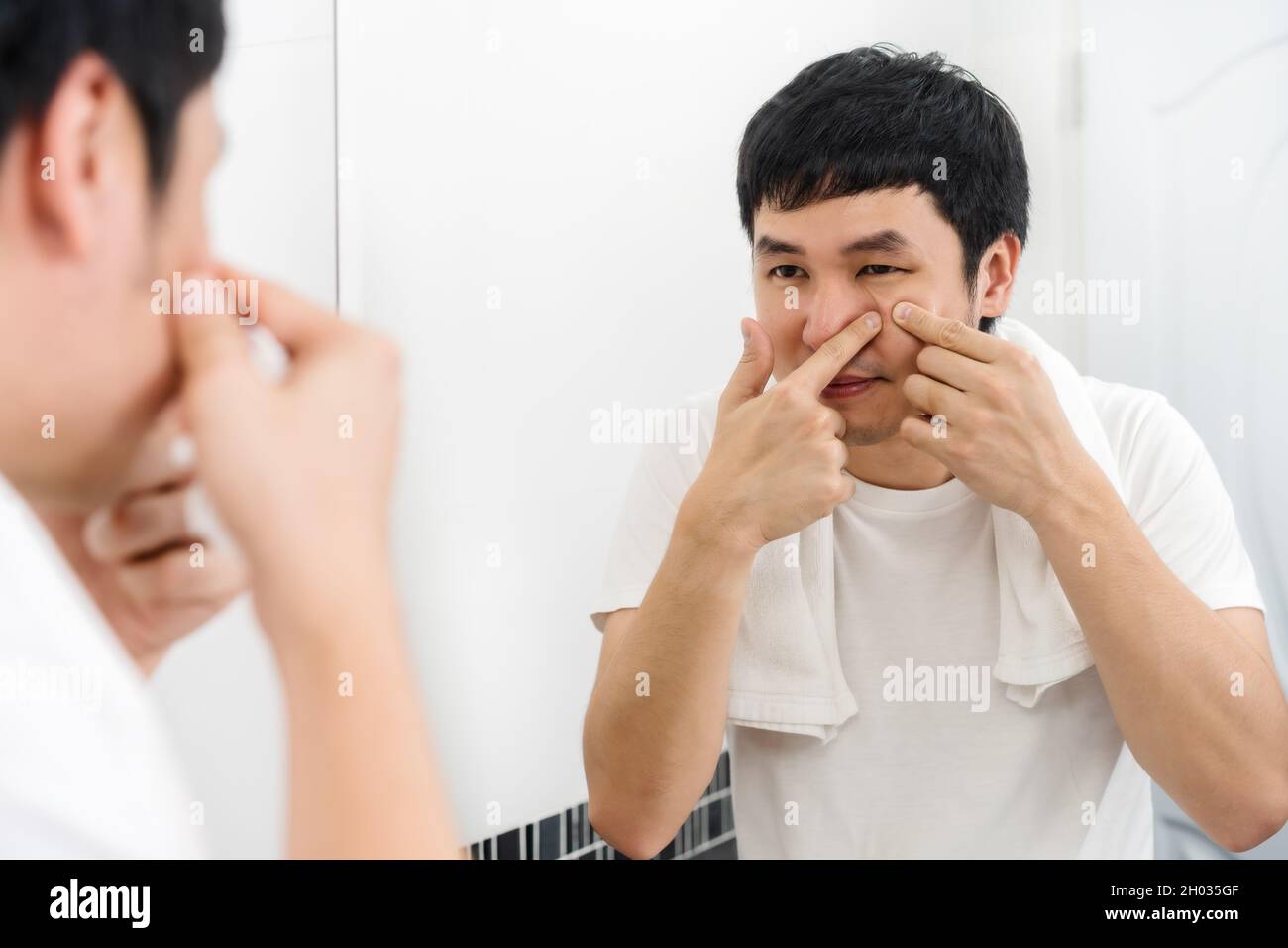 man squeezing a pimple in the bathroom mirror Stock Photo