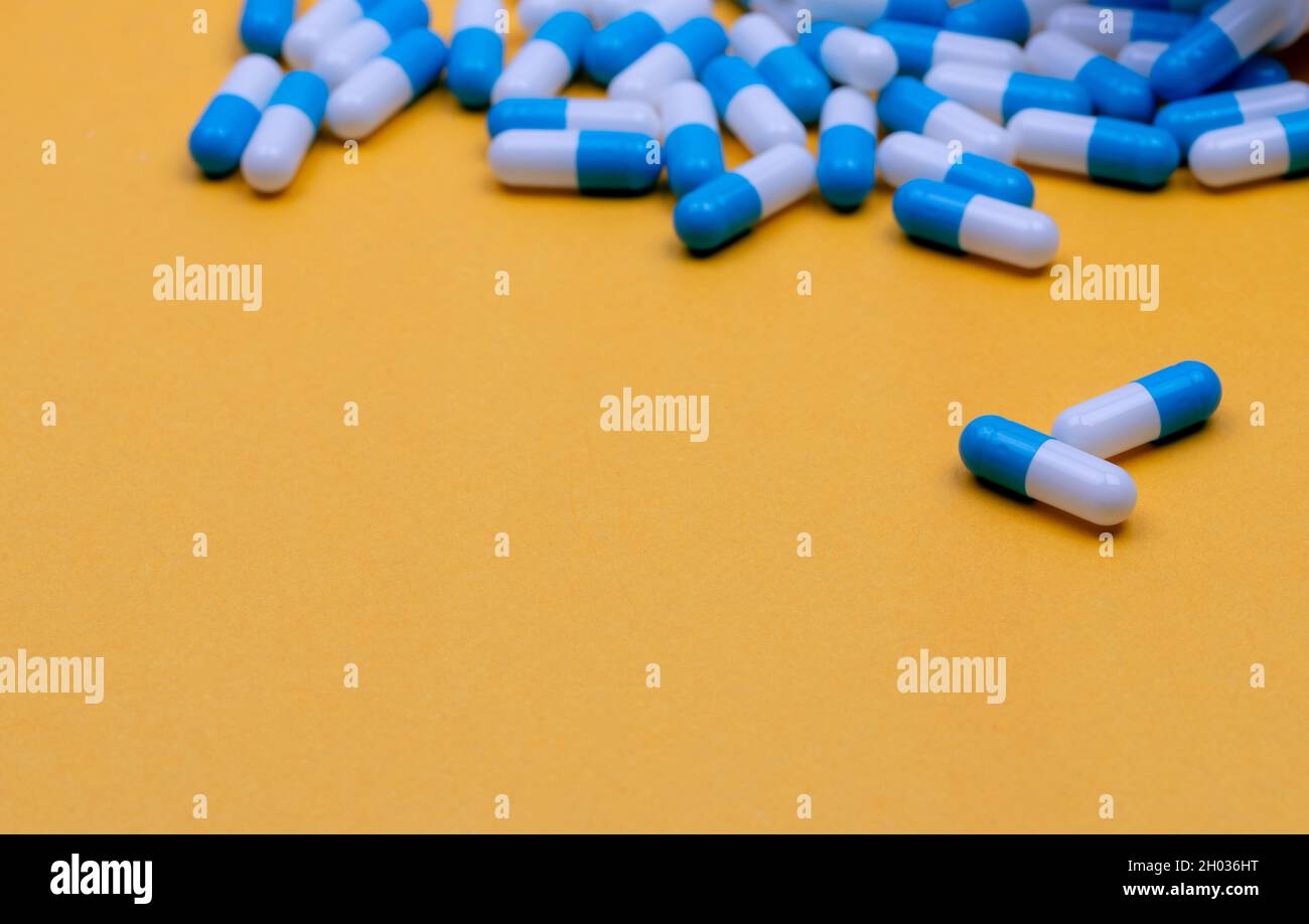 Blue and white antibiotic capsule pills spread on yellow background. Antibiotic drug resistance. Antimicrobial drug. Pharmaceutical industry. Pharmacy Stock Photo