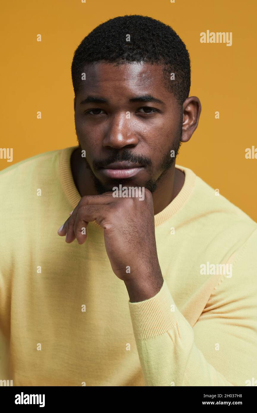 Vertical portrait of handsome African-American man looking at camera while posing resting chin on hand against yellow background in studio Stock Photo