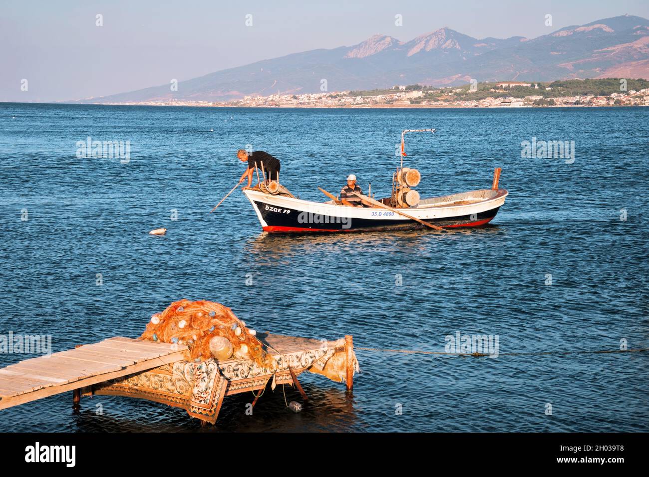 Urla, Turkey - September, 2021: Two Turkish fisherman on an old traditional fishing boat are approaching to the dock and cast anchor. Stock Photo